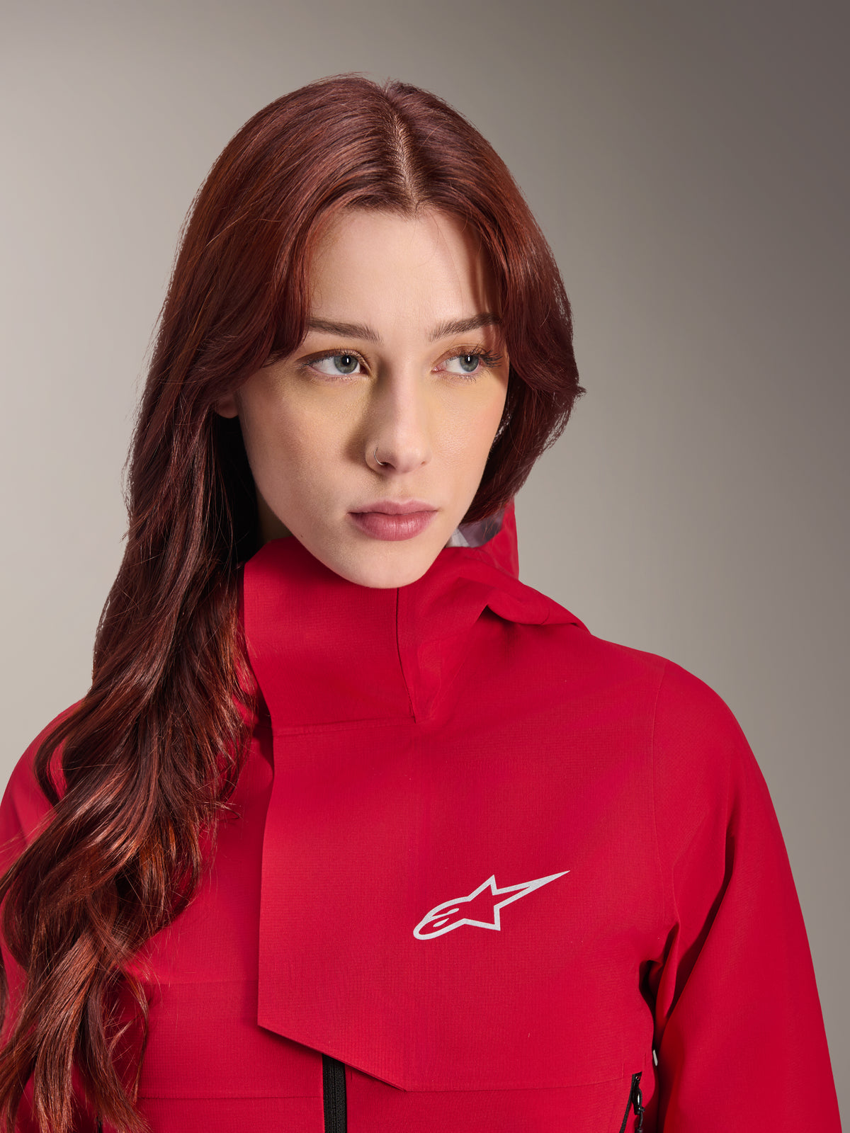 Veste imperméable Alpinestars Stella A-Dura Elite, Rouge Fluo, portée par une femme aux longs cheveux roux, veste technique imperméable 3 couches avec col haut et logo blanc, équipement de performance pour l'extérieur et le VTT