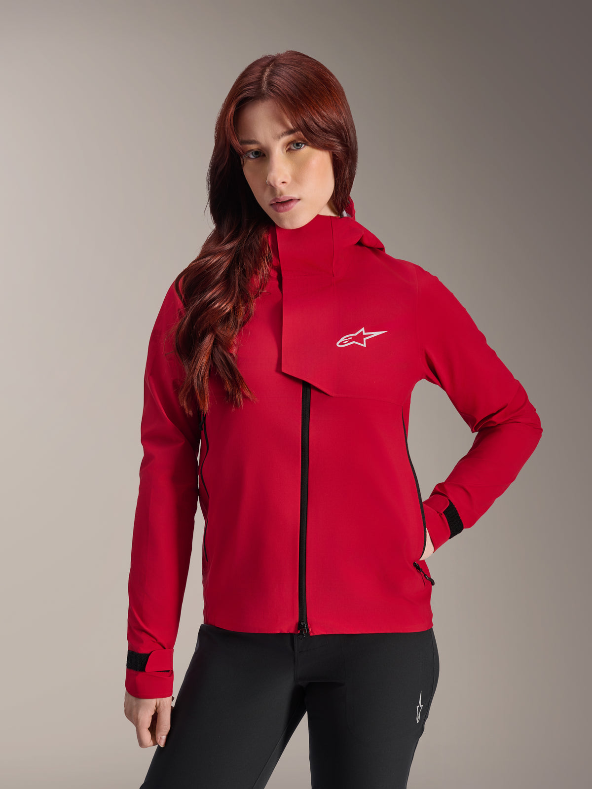 Veste imperméable Alpinestars Stella A-Dura Elite, veste de VTT pour femme, rouge fluo, dotée d'un rabat tempête frontal avec logo Alpinestars blanc, col montant et poignets réglables, portée avec un pantalon noir pour un look technique