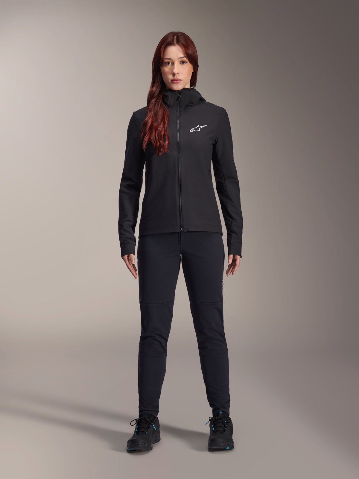 Veste thermique Alpinestars Stella A-Dura, noire, veste de cyclisme isolante légère pour femme avec capuche et logo Astars blanc sur la poitrine, accompagnée d'un pantalon noir et de chaussures de sport