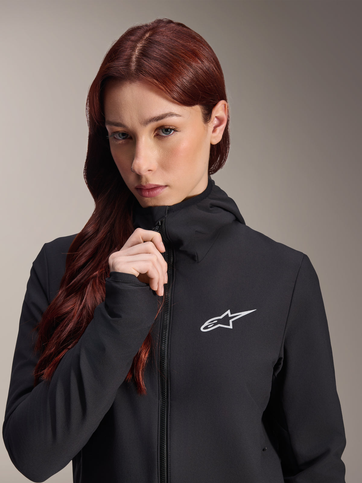 Veste thermique Alpinestars Stella A-Dura, veste de cyclisme noire pour femme, portée par un mannequin aux longs cheveux roux-brun, logo Alpinestars blanc sur la poitrine, design à capuche avec fermeture éclair intégrale, équipement de VTT