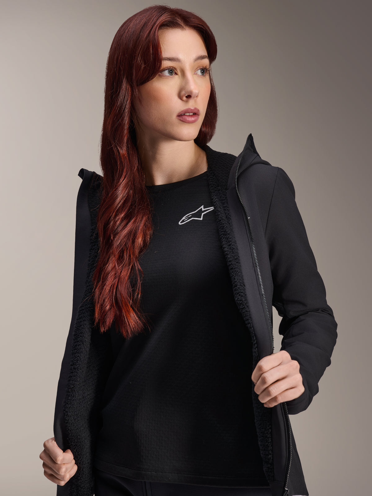 Veste thermique Alpinestars Stella A-Dura, veste de cyclisme noire pour femme, présentée ouverte avec une doublure en polaire texturée et une fermeture éclair à l'avant, portée par-dessus un t-shirt noir avec le logo Alpinestars, légère et isolée pour les sorties par temps froid