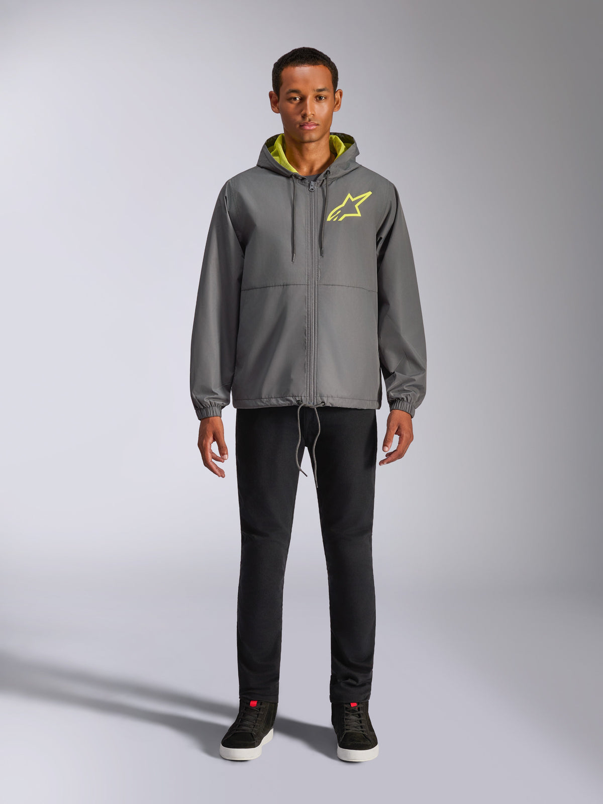 Alpinestars Speeder Chromium Windbreak Jacke, anthrazitgraue Kapuzenjacke mit neongelbem Innenfutter und Logo auf der Brust, durchgehender Frontreißverschluss, elastische Bündchen, lässige, vom Motorsport inspirierte Streetwear