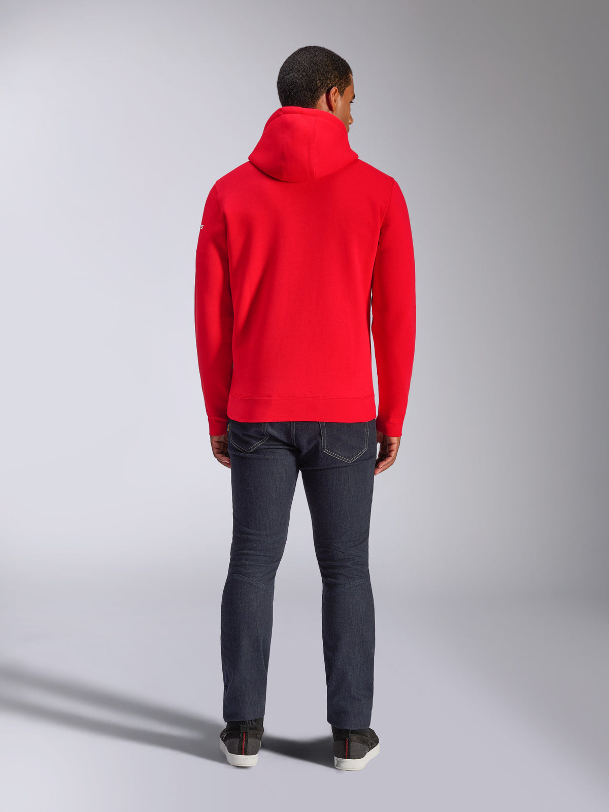 Alpinestars Frontal Hoodie, rode pullover fleece hoodie, achteraanzicht, casual streetwearstijl, gedragen met een donkere denim jeans en sneakers, voorzien van een capuchon en geribde boord