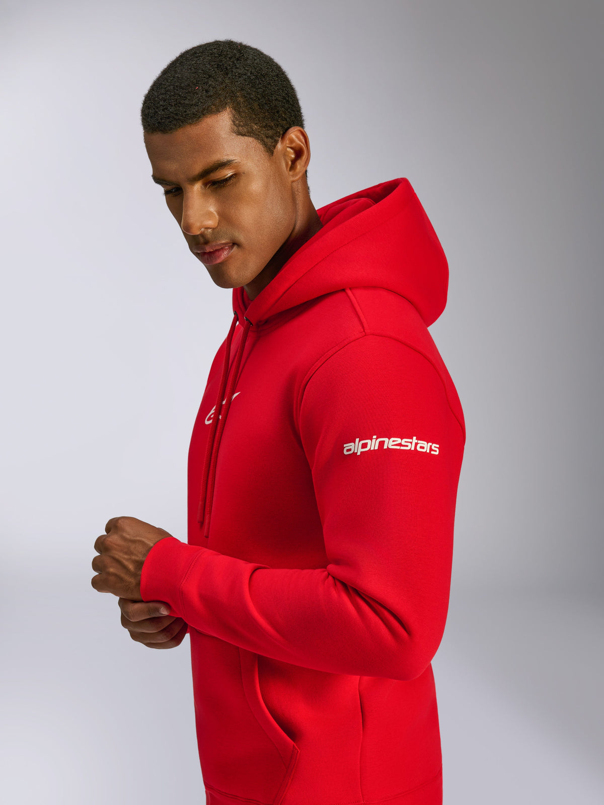 Alpinestars Frontal Hoodie, rood, fleece pullover hoodie gedragen door een model, met wit Alpinestars-woordmerk op de mouw, logo op de borst, kangoeroezak en capuchon met trekkoord, casual op motorsport geïnspireerd design