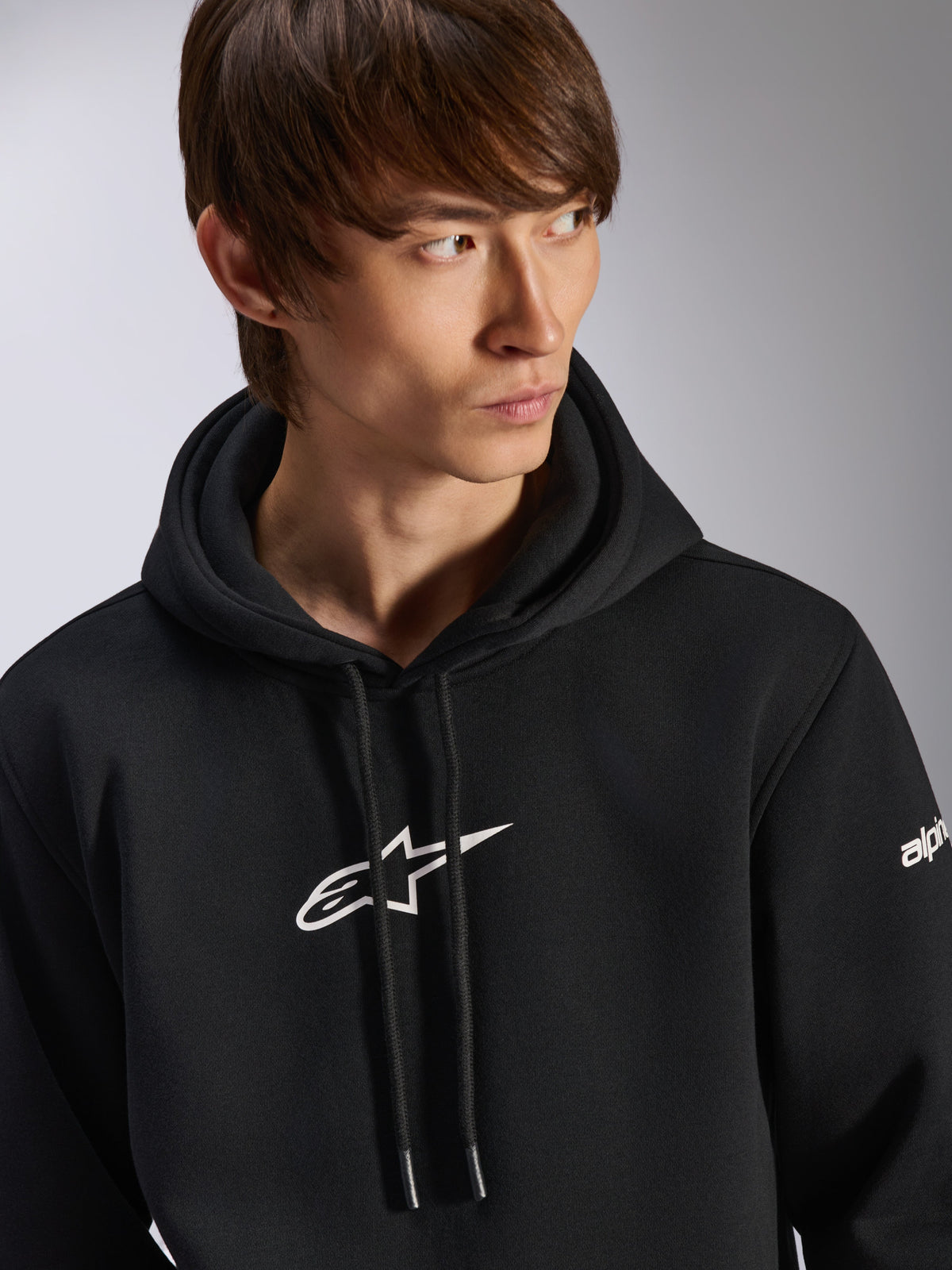 Alpinestars Frontal Hoodie, black pullover fleece hoodie, white Astar logo on chest and wordmark branding on sleeve, drawstring hood, worn by male model, casual motorsport streetwear