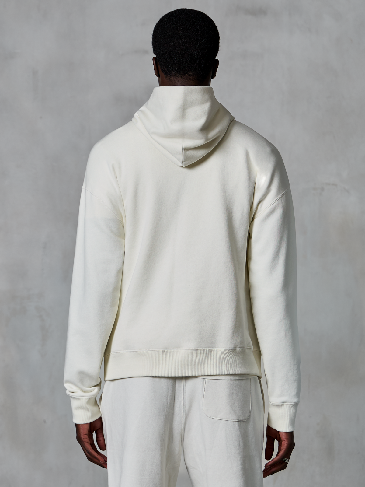 Alpinestars Essentials Ageless Hoodie, off-white pullover hoodie, achteraanzicht op model, strak minimalistisch design, bijpassende casual broek, ontspannen pasvorm voor dagelijks comfort
