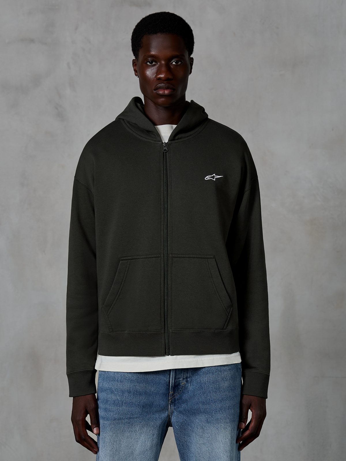 Alpinestars Essentials Ageless Zip Hoodie, sweat à capuche entièrement zippé, noir, avec un petit logo étoile blanc sur la poitrine, des poches avant et des poignets côtelés, porté comme vêtement décontracté d'inspiration sport mécanique
