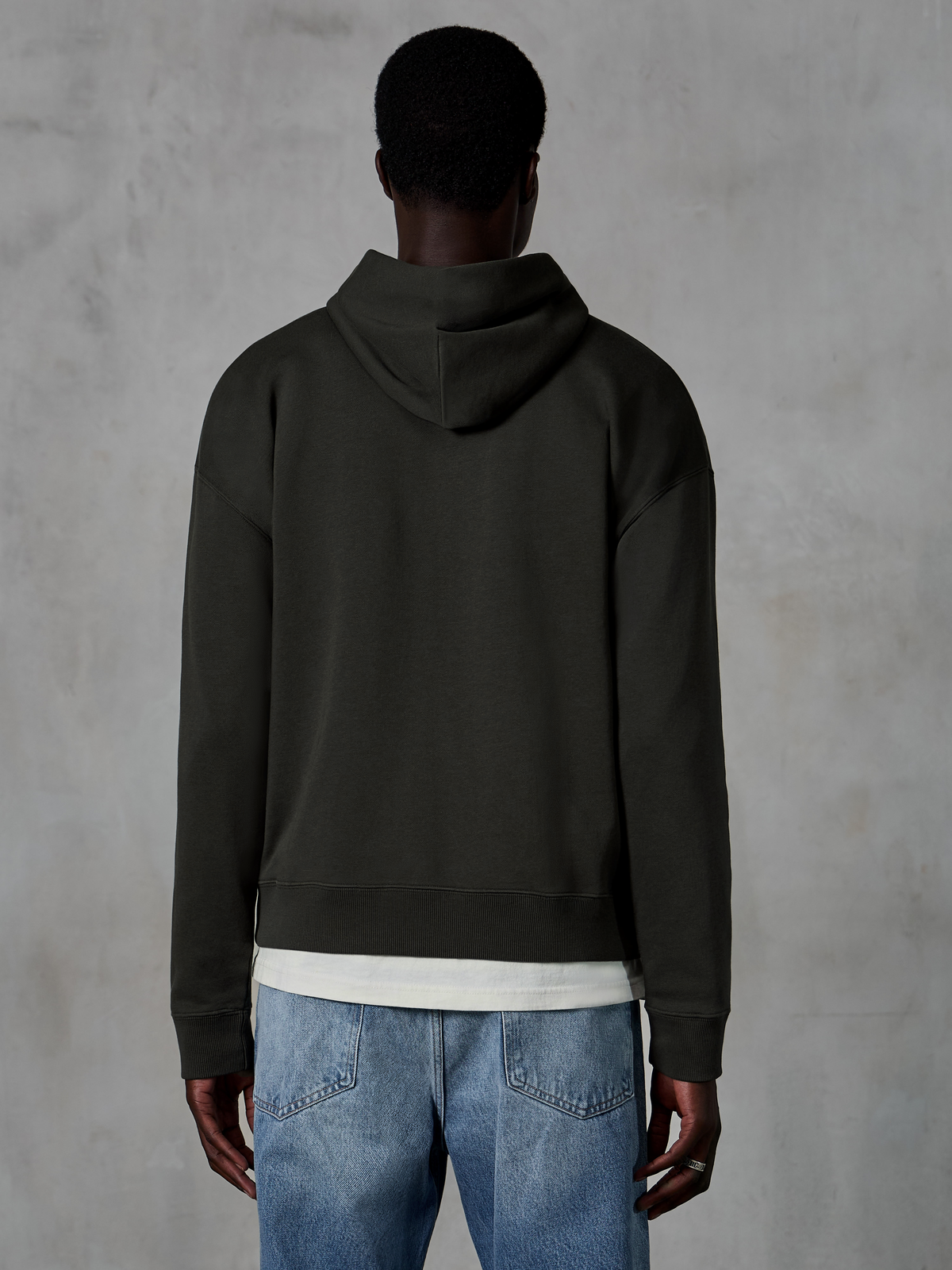 Alpinestars Essentials Ageless Zip Hoodie, vue de dos d'un sweat à capuche à coupe décontractée en coloris Off Black, porté avec un t-shirt blanc et un jean bleu, vêtement de sport épuré et discret d'inspiration sport automobile.