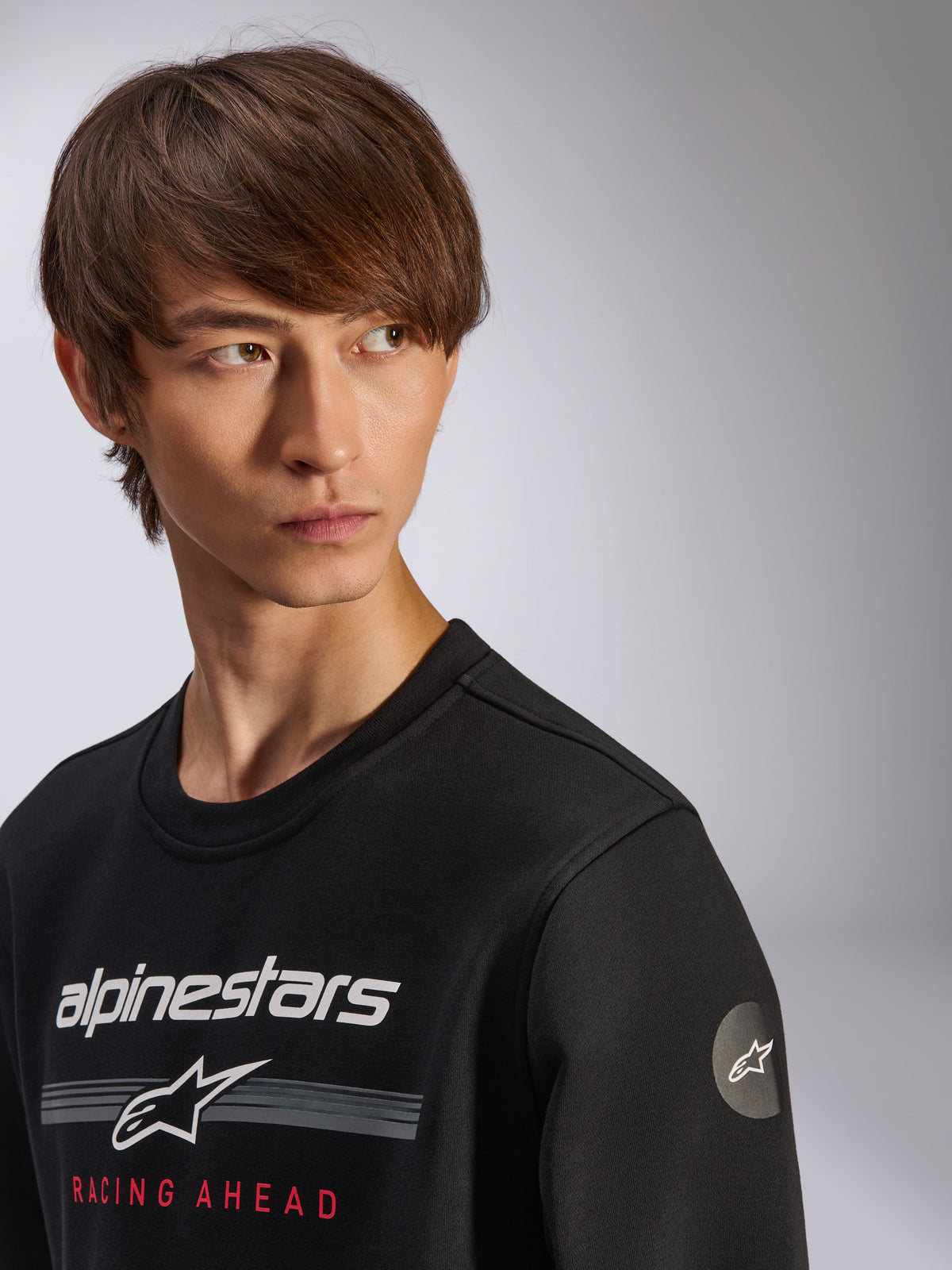 Alpinestars Bettern Crew Sweatshirt, Schwarz, mit weißem Alpinestars-Logo, grauen Streifen und rotem „RACING AHEAD“-Schriftzug, kreisförmiges Stern-Logo am Ärmel, lässige, vom Motorsport inspirierte Streetwear