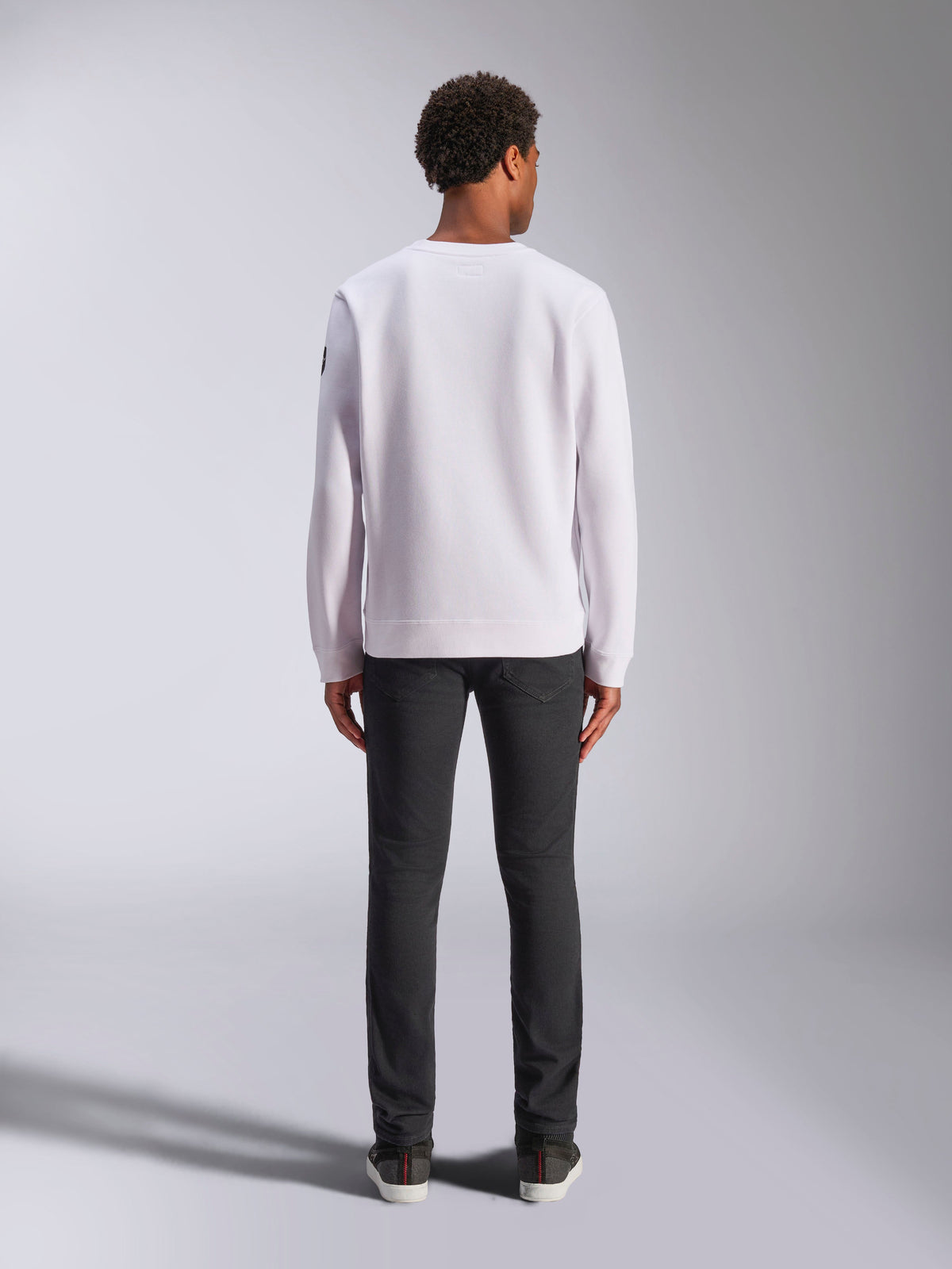 Alpinestars Bettern Crew, sweat à col rond blanc, vue de dos sur mannequin, porté avec un jean foncé et des baskets, style streetwear décontracté d'inspiration sport automobile