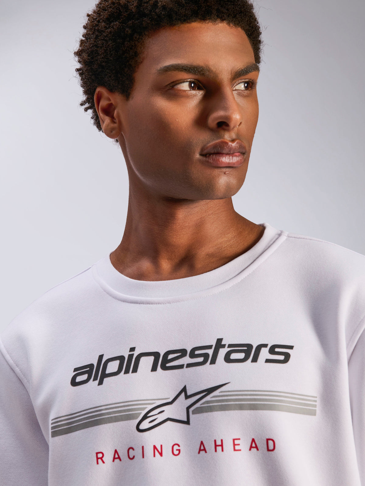 Alpinestars Bettern Crew, sweat à col rond en polaire blanche, logo Alpinestars noir avec lignes horizontales grises et texte 'Racing Ahead' rouge, vêtement streetwear décontracté inspiré du sport automobile