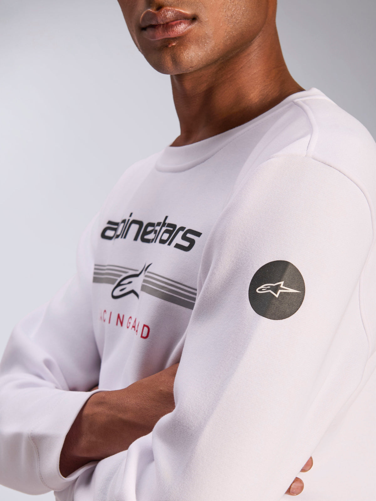 Alpinestars Bettern Crew, sweatshirt à col rond blanc, vêtement streetwear décontracté inspiré du sport automobile, avec graphisme sur la poitrine, lettrage Alpinestars et rayures grises, patch logo étoilé circulaire noir sur la manche, modèle en polaire