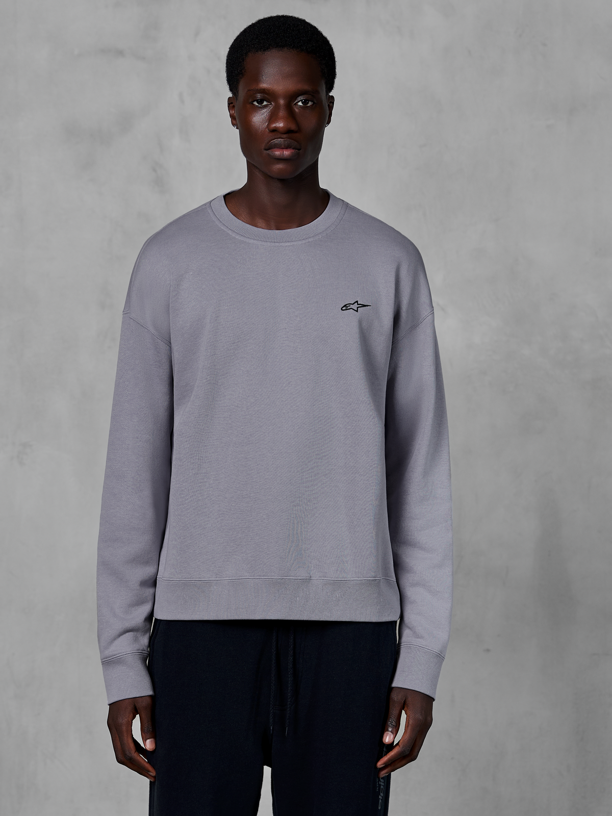 Alpinestars Essentials Ageless Crew, zilverkleurige sweatshirt met ronde hals gedragen door een model, voorzien van een klein zwart sterlogo op de borst, ontspannen pasvorm met geribbelde manchetten en zoom, casual motorsport streetwear