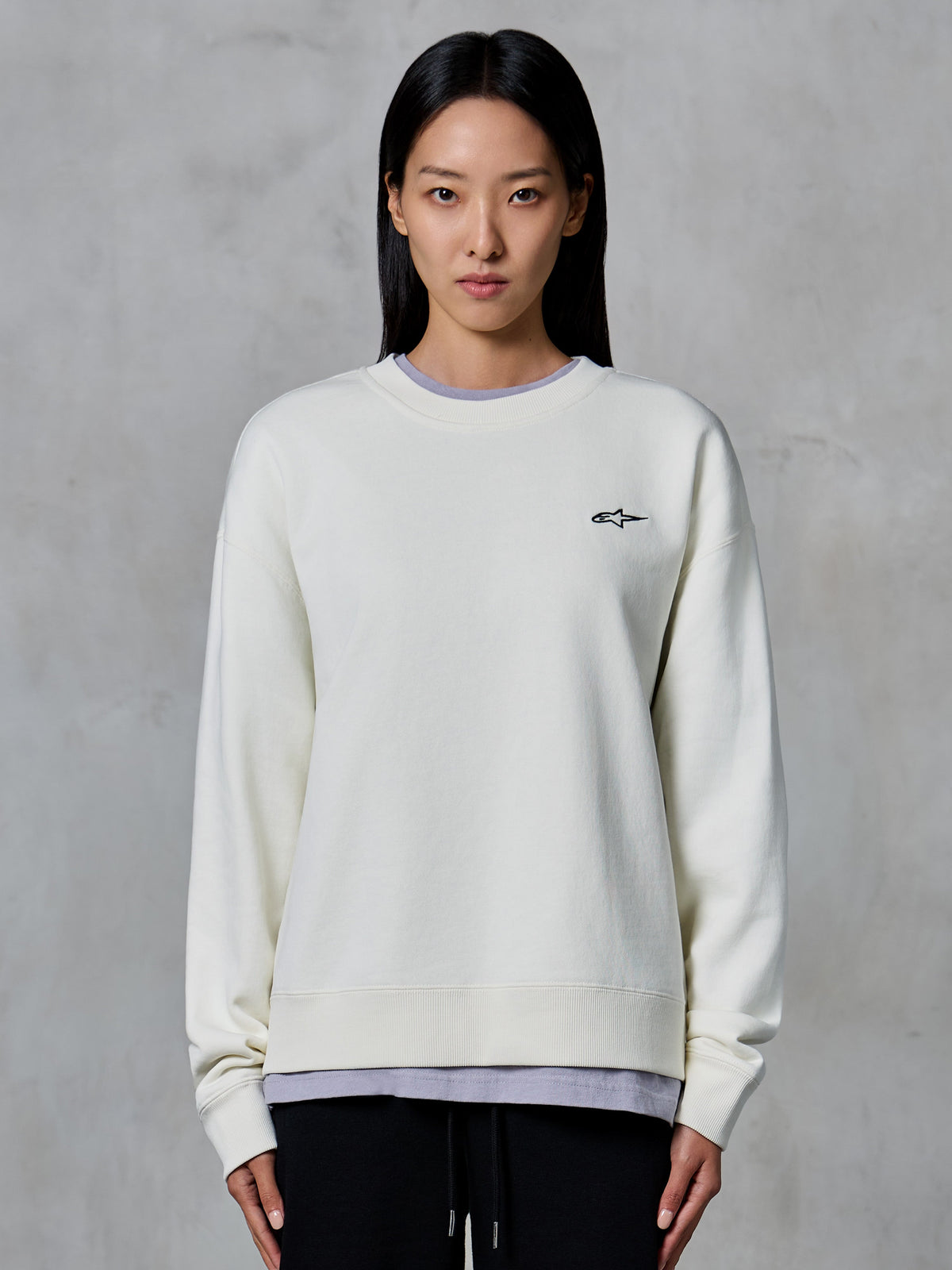 Alpinestars Essentials Ageless Crew, crewneck sweatshirt, off-white, met een klein zwart Alpinestars logo op de borst, casual lifestyle kleding gedragen door een vrouw