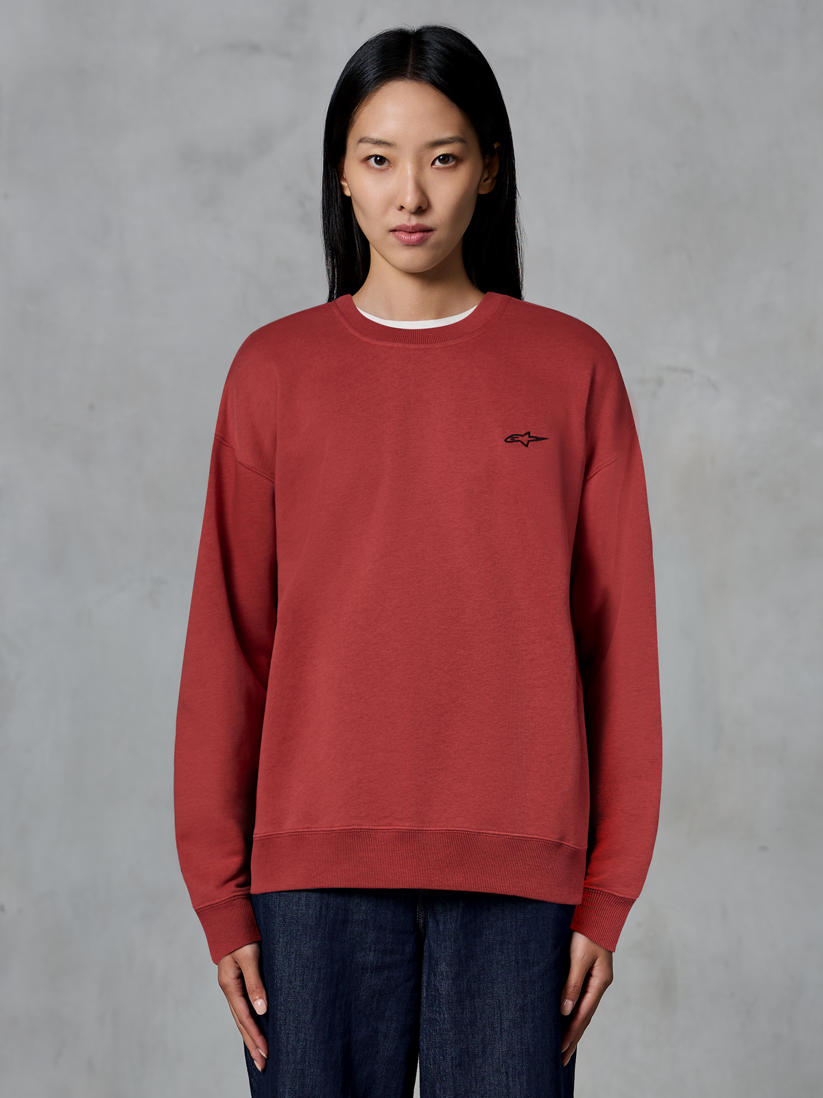 Alpinestars Essentials Ageless Crew, sweat-shirt à col rond rouge brique, petit logo noir sur la poitrine, polaire de qualité supérieure, porté par un mannequin, streetwear décontracté inspiré du sport automobile