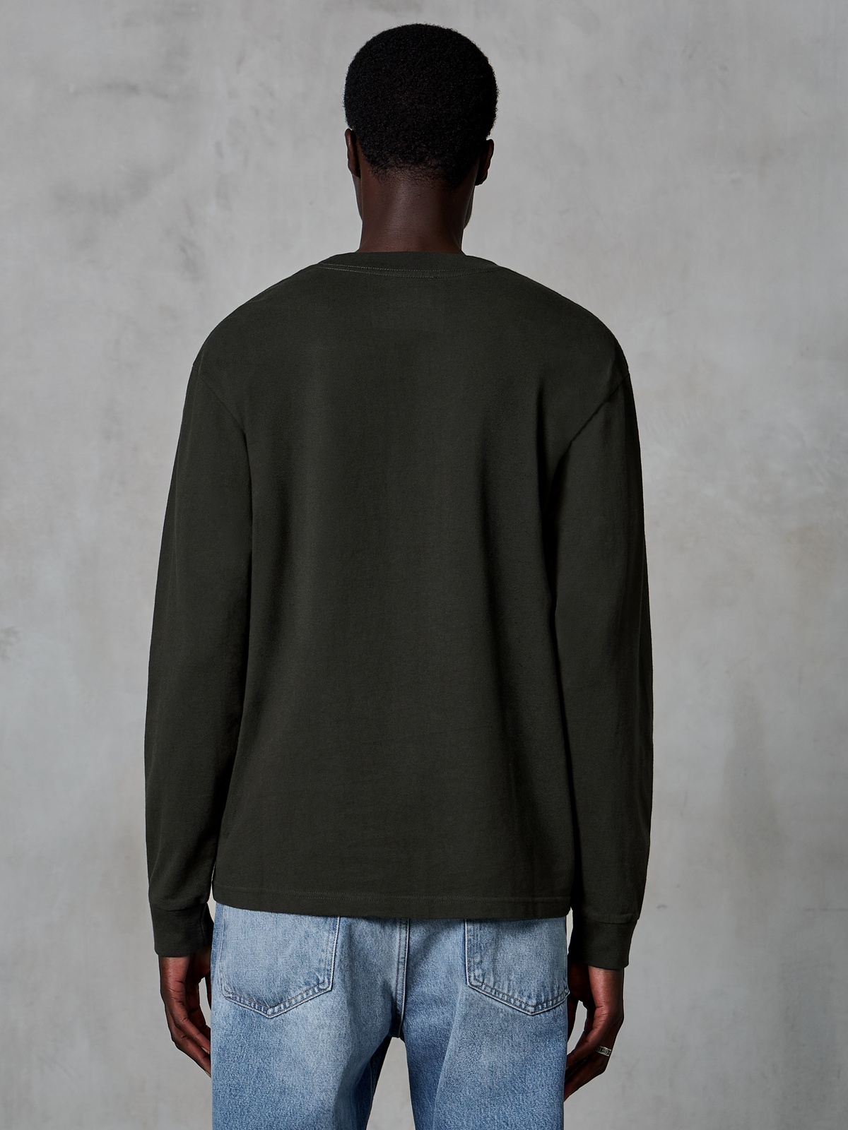Alpinestars Essentials Ageless LS Tee, T-shirt met lange mouwen, Off Black, achteraanzicht met een strak ontwerp en ontspannen pasvorm, gedragen door model met blauwe jeans, casual streetwear geïnspireerd op de motorsport