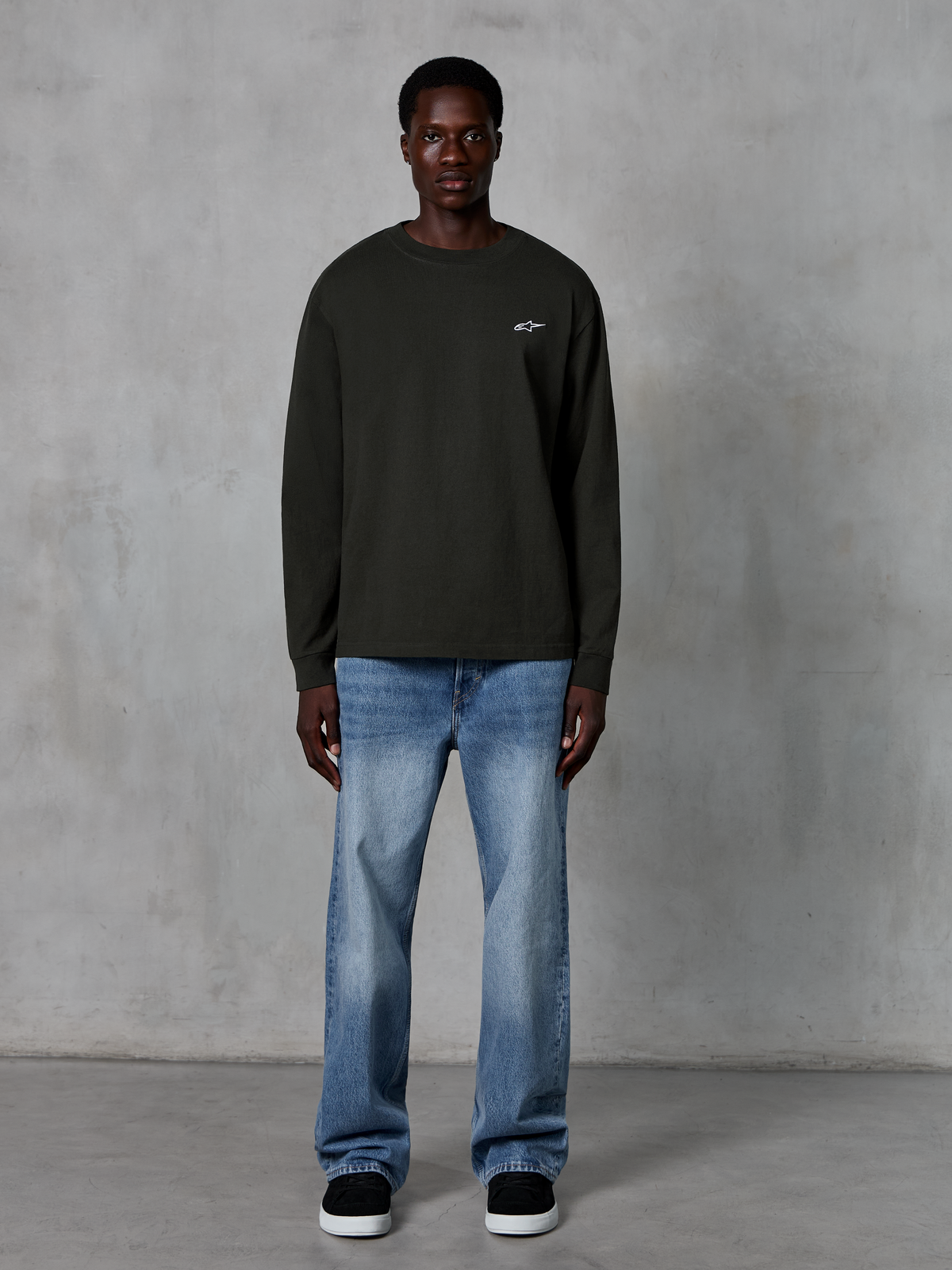 Alpinestars Essentials Ageless LS Tee, T-shirt met lange mouwen, Off Black, voorzien van een klein wit sterlogo op de borst, ontspannen pasvorm, casual motorsport streetwear, gecombineerd met een lichtblauwe jeans