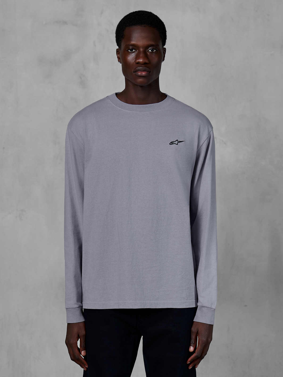 T-shirt à manches longues Alpinestars Essentials Ageless, argent, porté par un mannequin, avec un petit logo Alpinestars noir sur la poitrine, coupe décontractée contemporaine, streetwear décontracté en coton biologique