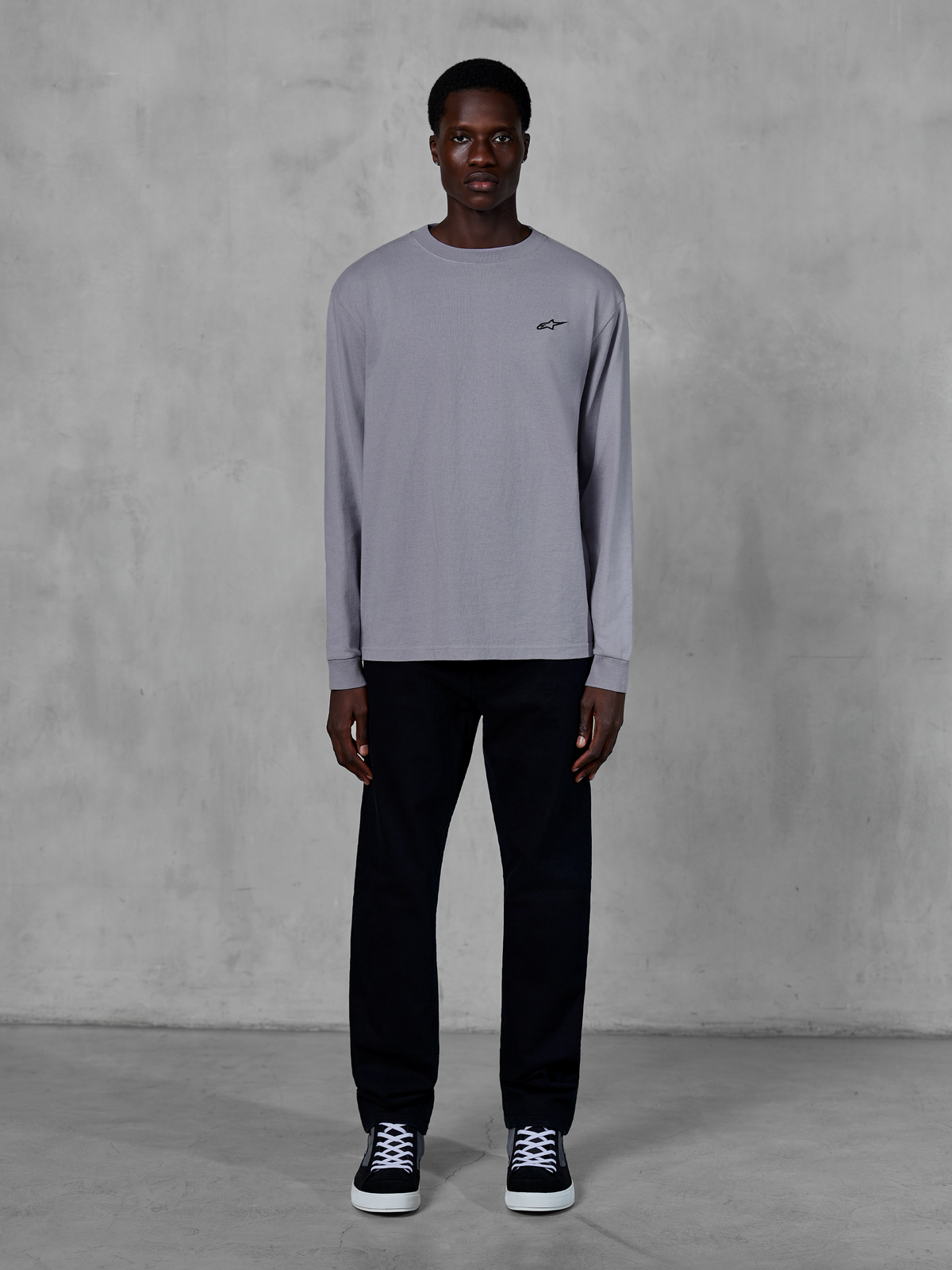 Alpinestars Essentials Ageless LS Tee, t-shirt à manches longues, argent, petit logo Alpinestars noir sur la poitrine, jersey en coton biologique avec finition stone wash, porté par un mannequin avec un pantalon noir et des baskets, style streetwear décontracté