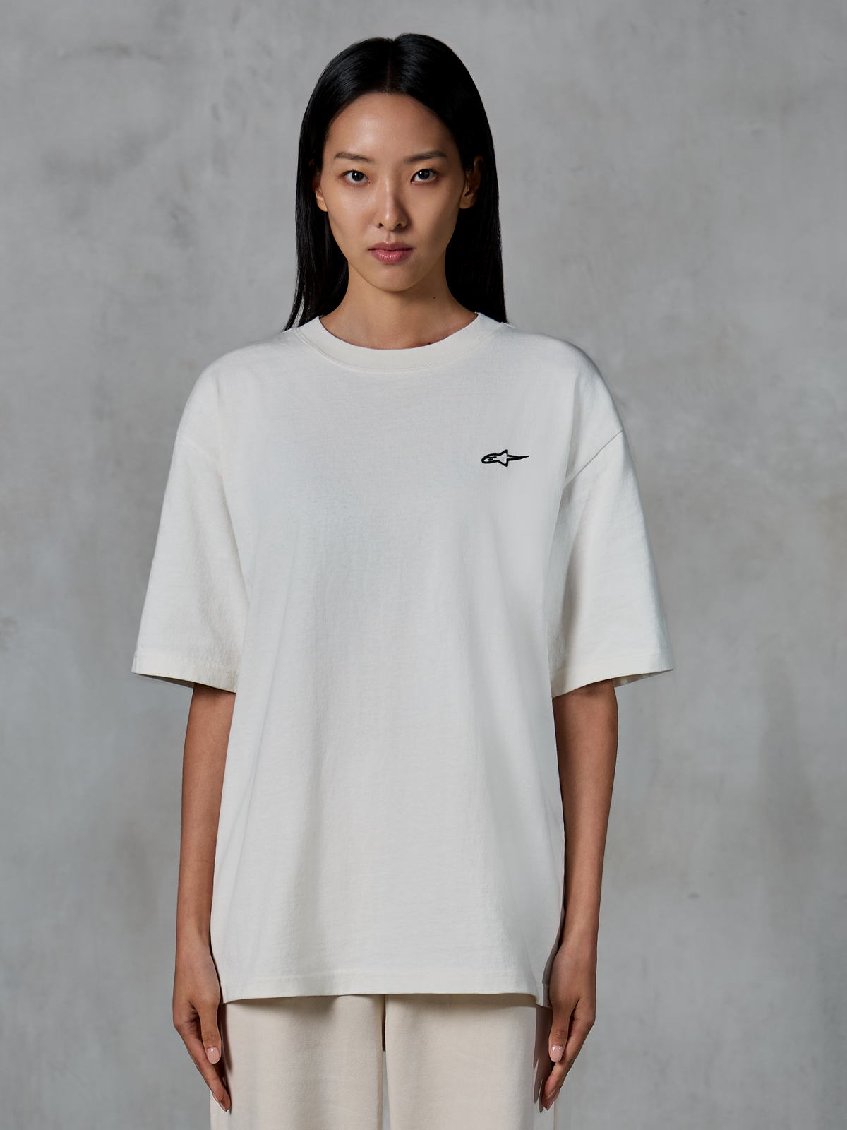 Alpinestars Essentials Ageless SS Tee, t-shirt à manches courtes, blanc cassé, porté par un mannequin femme, avec un petit logo Alpinestars noir sur la poitrine, coupe décontractée, style streetwear décontracté