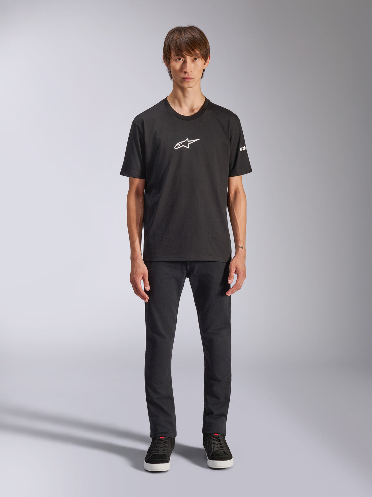 Alpinestars Frontal CSF T-Shirt, Kurzarm-T-Shirt, Schwarz, weißes Alpinestars-Logo auf der Brust, getragen von einem Model mit schwarzer Hose und schwarzen Schuhen, lässige Performance-Sportbekleidung