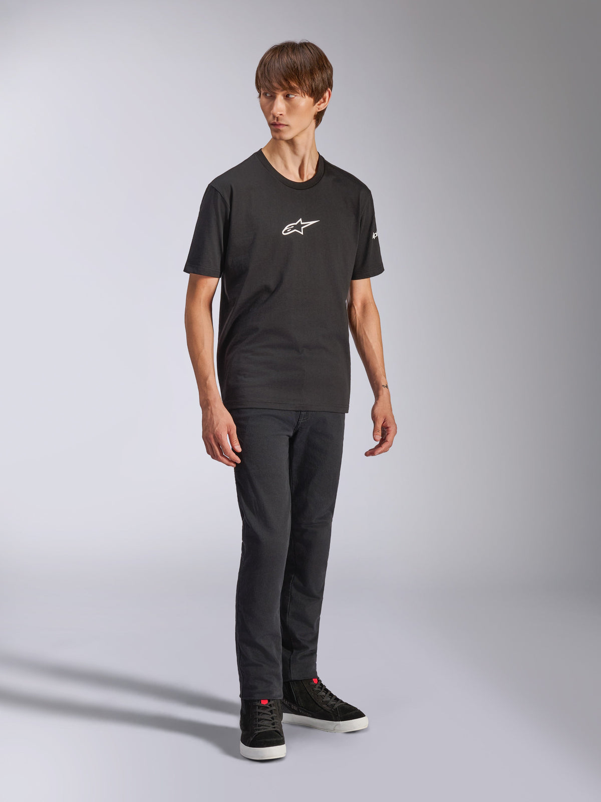 Alpinestars Frontal CSF Tee, Kurzarm-T-Shirt, Schwarz, weißes Astars-Logo auf der Brust, getragen von einem Model mit dunkler Jeans und schwarzen Sneakern, lässige Performance-Streetwear
