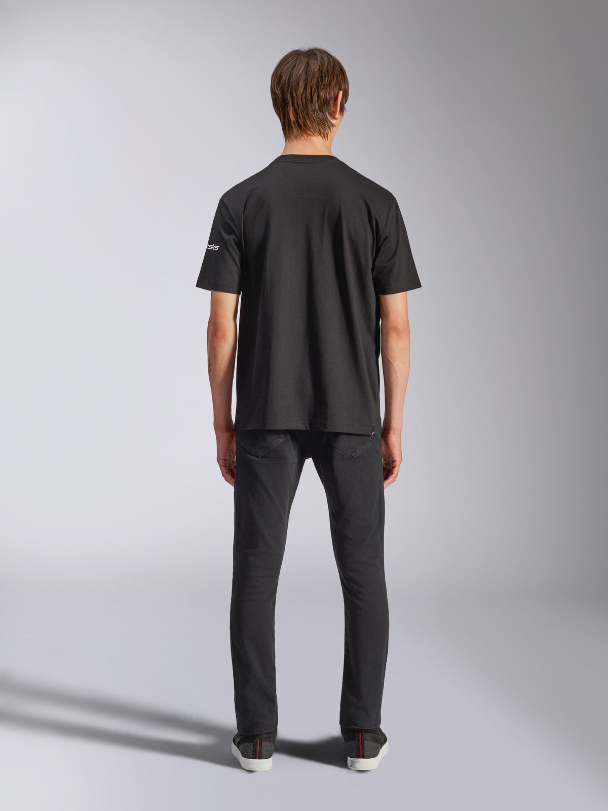 Alpinestars Frontal CSF T-Shirt, Kurzarm, Schwarz, Rückansicht am Model in schwarzen Jeans, lässige Performance-Streetwear mit kleinem weißem Logo-Detail am Ärmel