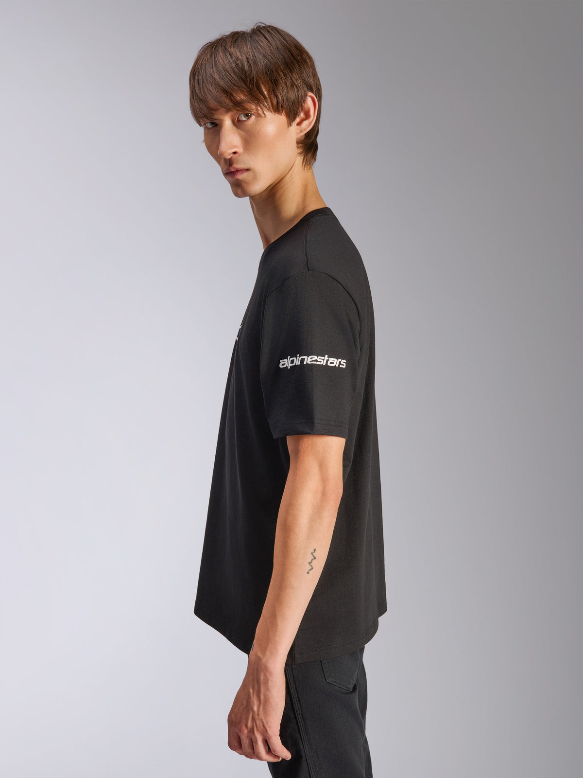 Alpinestars Frontal CSF Tee, Kurzarm-T-Shirt, Schwarz, weißes Alpinestars-Logo auf dem Ärmel, von einem Modell in der Profilansicht getragen, lässige Motorsport-Performance-Streetwear