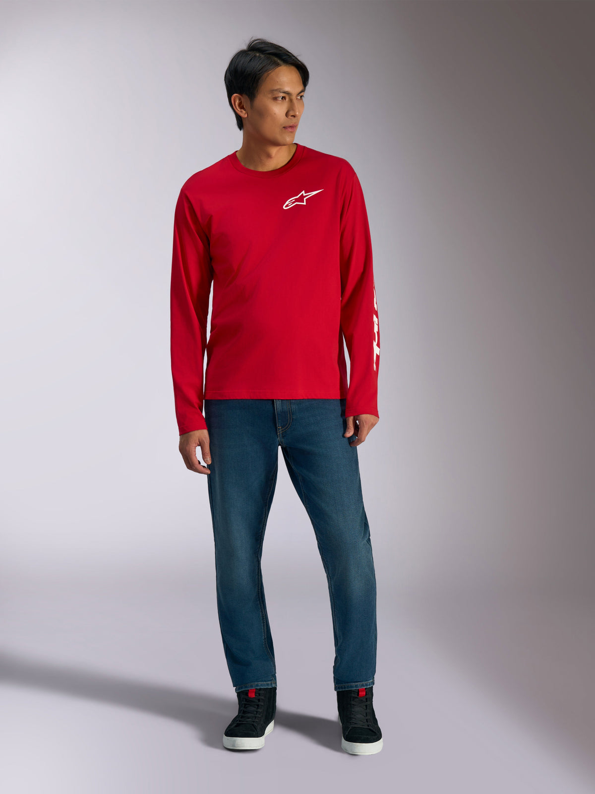 Alpinestars Trackside CSF Tee, Langarmshirt, Rot mit weißem Alpinestars-Logo, Lifestyle-Aufnahme getragen mit blauen Jeans und schwarzen Sneakern, lässige, vom Motorsport inspirierte Sportbekleidung