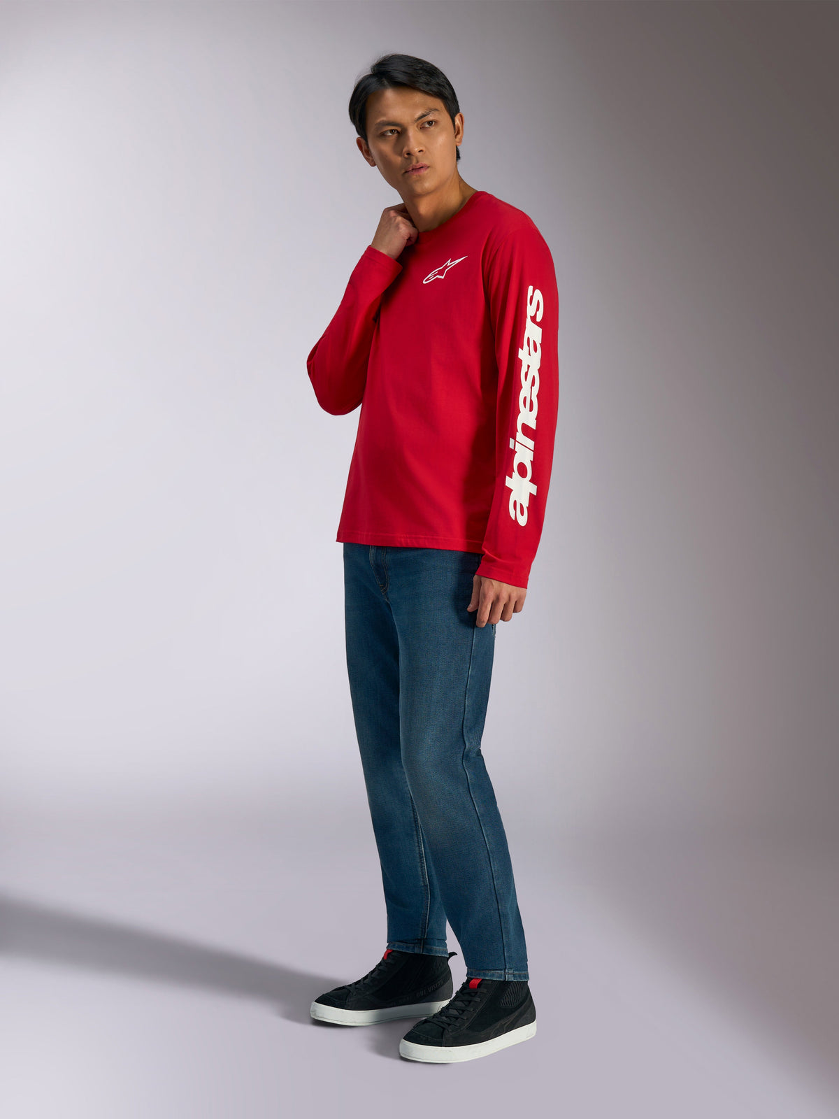Alpinestars Trackside CSF Langarmshirt, Rot mit weißem Alpinestars-Branding auf Brust und Ärmel, getragen von einem Model mit blauen Jeans und schwarzen Sneakern, lässige, vom Motorsport inspirierte Streetwear
