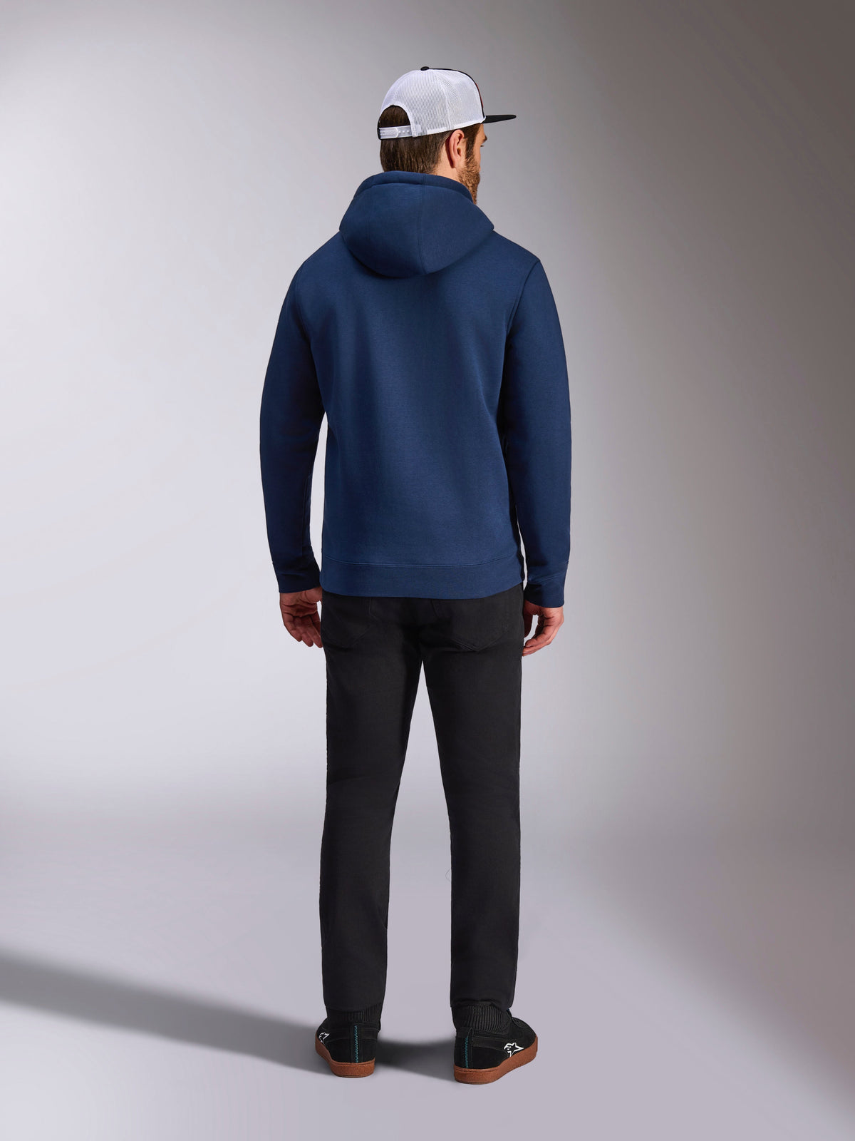 Alpinestars Frontal Hoodie, bleu marine, vue de dos d'un homme portant un sweat à capuche décontracté en polaire avec poignets et ourlet côtelés, associé à un pantalon noir et une casquette blanche en mesh, streetwear d'inspiration sport automobile