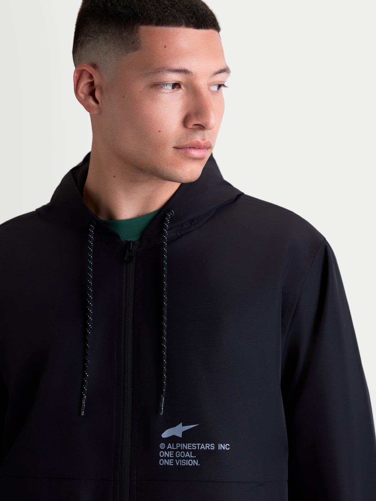 Alpinestars Veste Coupe-Vent Speeder Resolve, veste à capuche légère pour homme, noire, style sportswear urbain, vue rapprochée avec logo sur la poitrine et cordons de serrage mouchetés.
