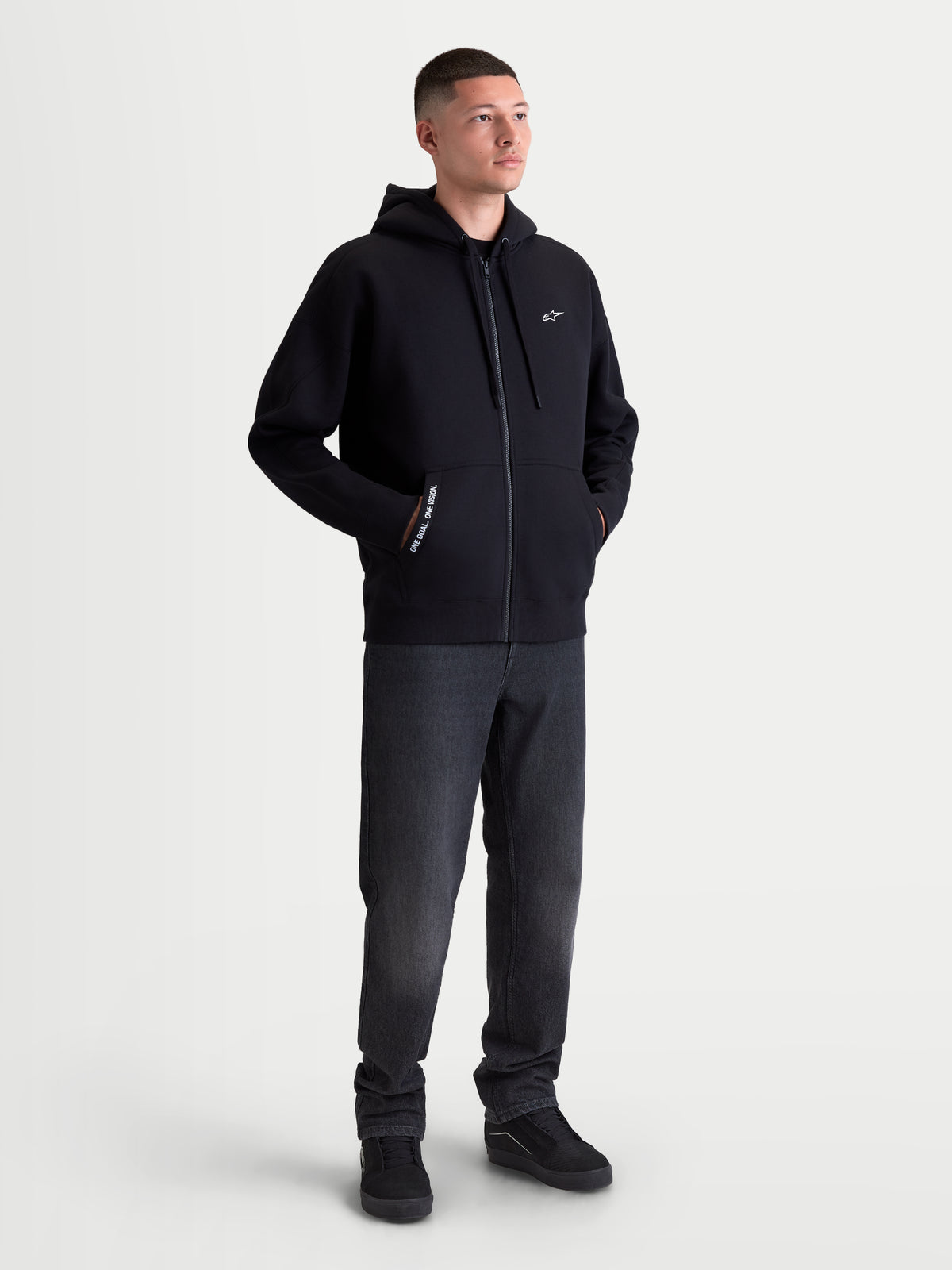 Alpinestars sweat à capuche Pioneer Oversize, polaire zippée sportswear pour homme, noir avec logo Astars blanc sur la poitrine, fermeture éclair Vislon et poche kangourou. Vue sur mannequin montrant la coupe décontractée oversize conçue pour un look casual quotidien.