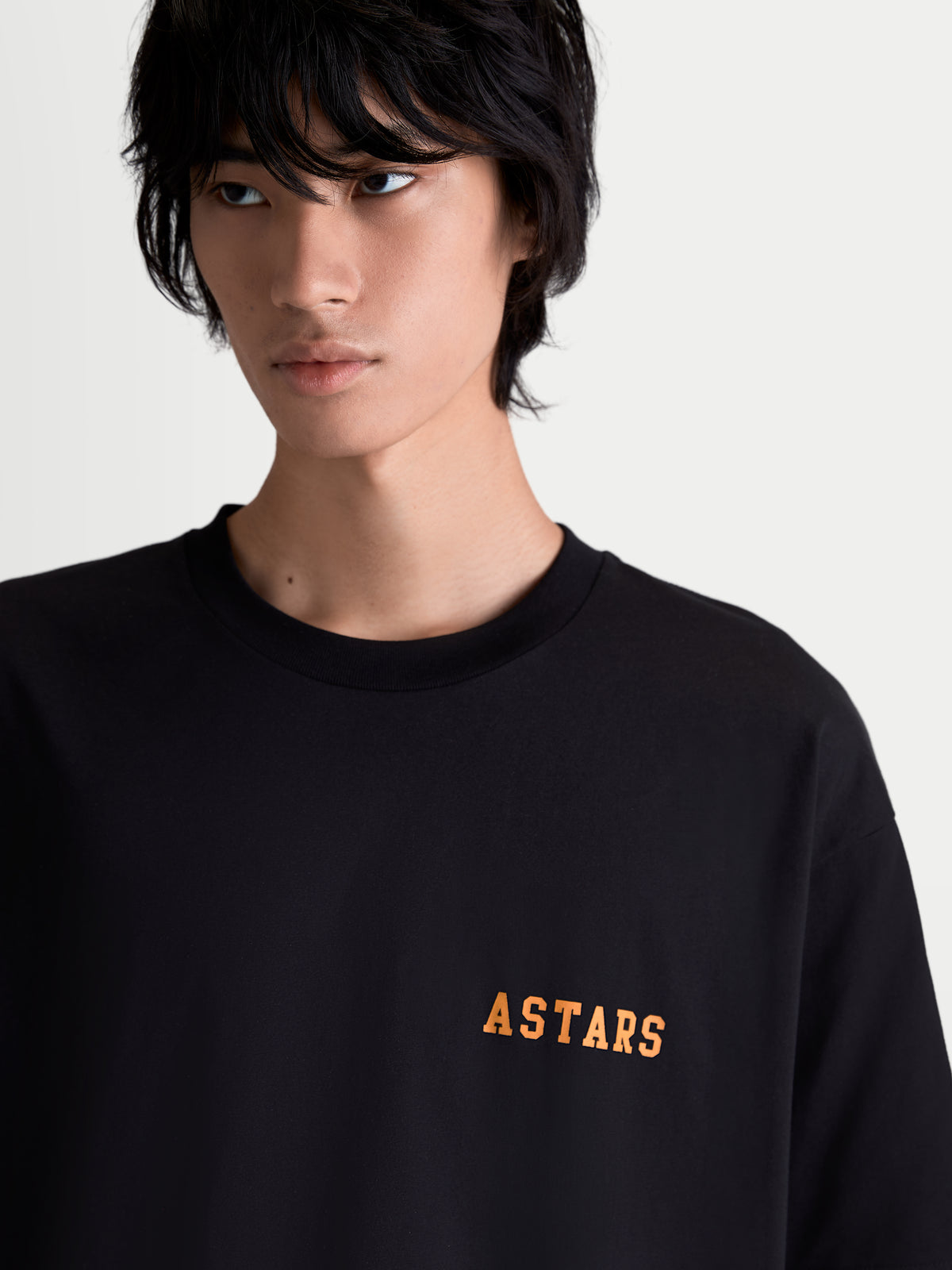 Alpinestars Latitude Oversized CSF T-Shirt, Kurzarm-Sportswear-T-Shirt, Unisex, Schwarz und Orange, Baumwoll-Polyester-Mischung, Vorderansicht am Model mit weicher ASTARS-Wortmarken-Grafik auf der Brust.