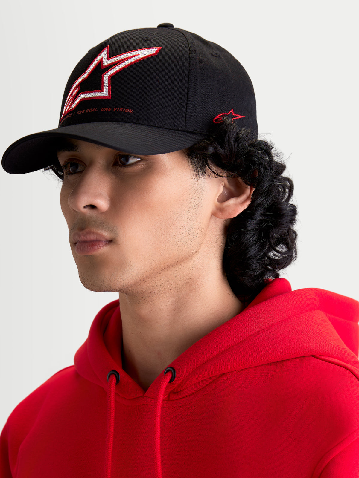 Alpinestars Lineout Kappe, schwarze Sportswear-Kappe mit gebogenem Schirm, getragen von einem Model. Die Kappe verfügt über eine strukturierte Krone mit rot-weiß gesticktem Astars-Logo und seitlichem Branding.