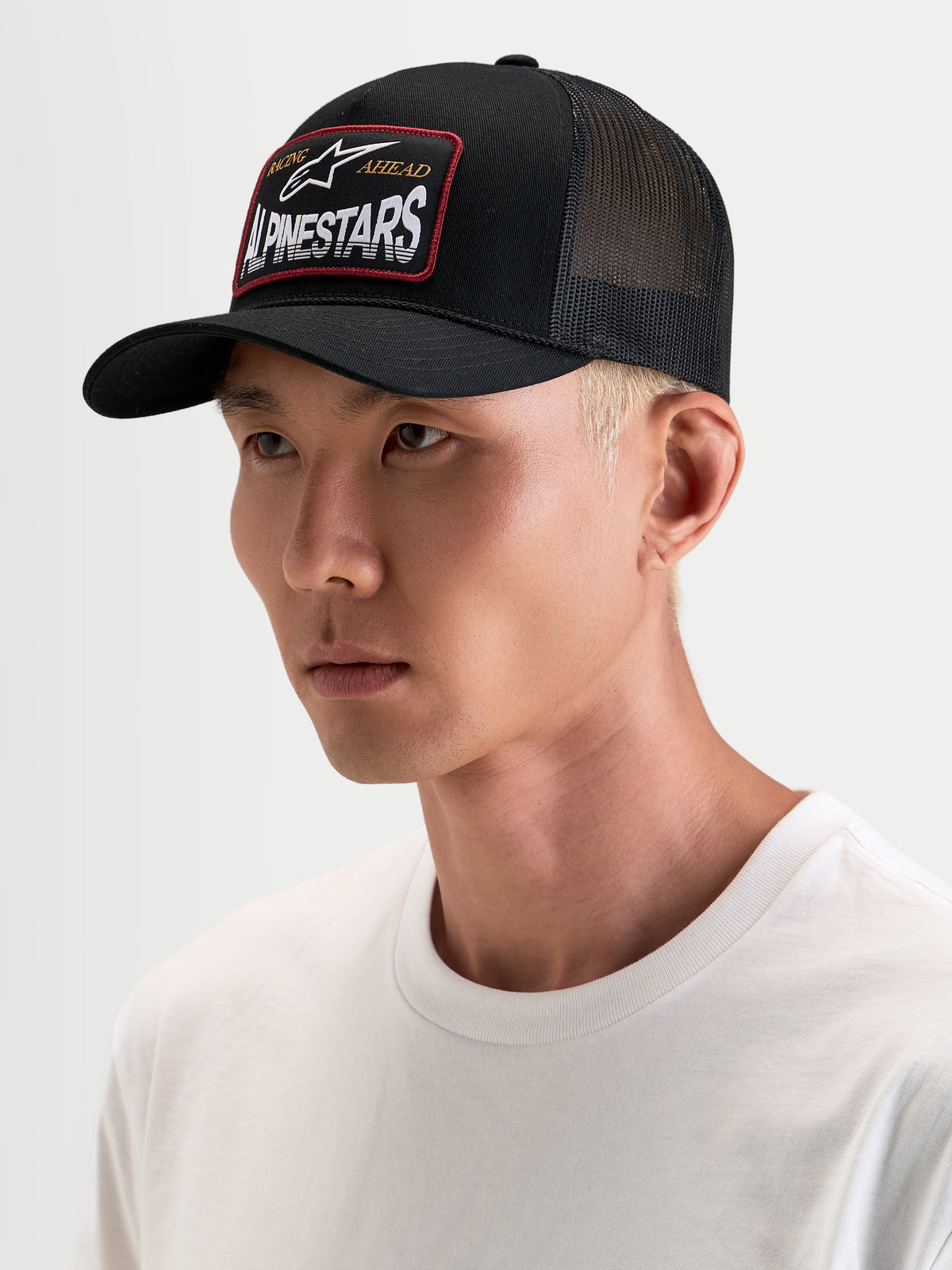 Casquette Trucker Hemmings d'Alpinestars, casquette trucker sportswear noire portée par un modèle, avec des empiècements en mesh respirant à l'arrière et un écusson tissé du logo sur le devant