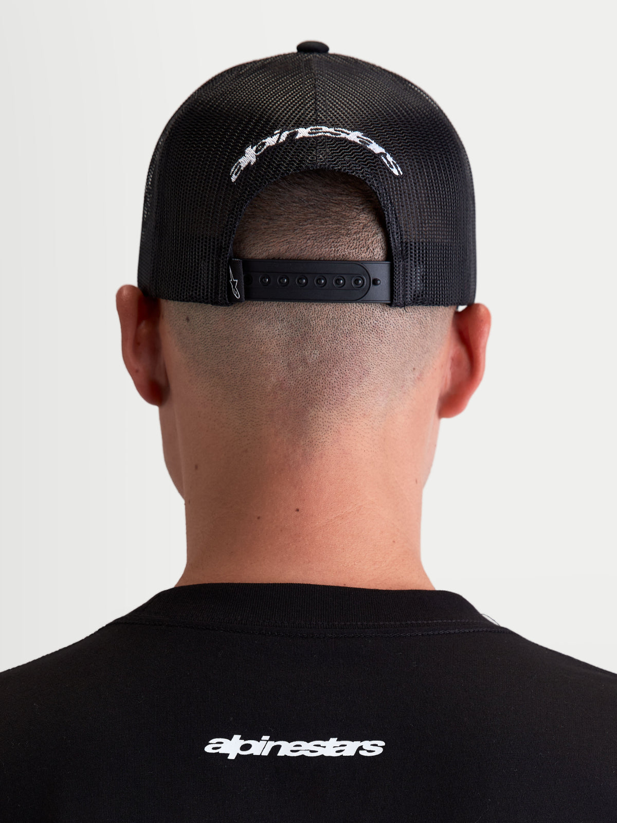Alpinestars Casquette Trucker Meteorite, casquette de sportswear noire et blanche, vue de dos montrant l'arrière en maille respirante, la fermeture snapback ajustable et le logo Alpinestars brodé en blanc.