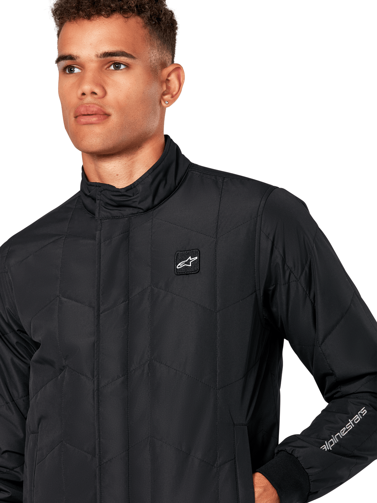 Alpinestars Precedent Jacke, gesteppte Sportswear-Jacke für Herren in Schwarz, Nahaufnahme mit niedrigem Stehkragen, Logo-Patch auf der Brust und Ärmelstickerei, ikonisches schräges Steppmuster für einen vom Motorsport inspirierten Look.