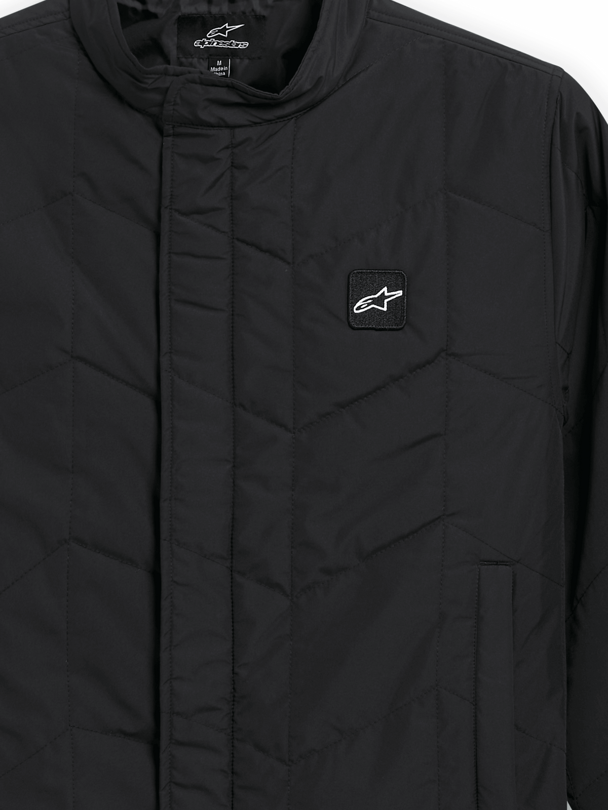 Alpinestars Precedent Jacke, gesteppte Sportswear-Jacke, Schwarz, Nahaufnahme mit ikonischem schrägem Steppmuster, niedrigem Stehkragen, verdecktem Frontreißverschluss und kleinem Logo-Patch auf der Brust