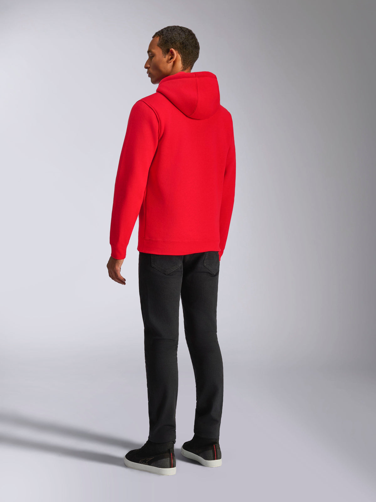 Alpinestars Ageless V3 Hoodie, casual streetwear, levendig rood, achteraanzicht van model, met jersey-gevoerde capuchon, geribde boorden en zoom, gecombineerd met zwarte broek, modern motorsport-geïnspireerd ontwerp.