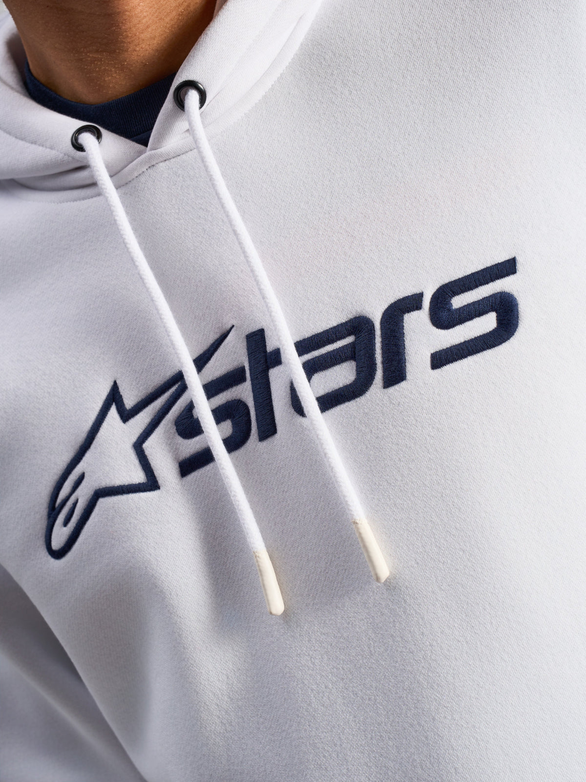 Sweat à capuche Alpinestars Blaze V3, blanc et bleu marine, gros plan sur la poitrine avec logo imprimé bleu marine à l'avant et cordons de serrage blancs à embouts trempés, vêtement streetwear décontracté motorsport