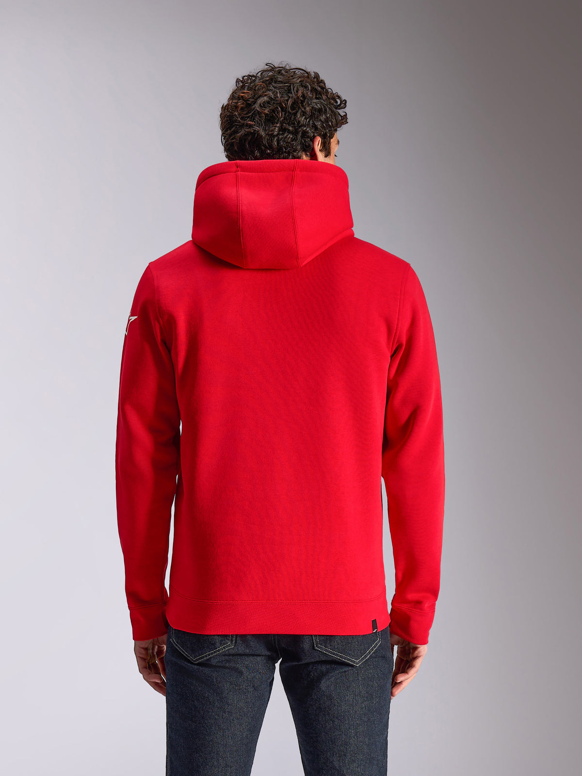 Alpinestars Linear Wordmark V3 Hoodie, achteraanzicht van een rode hoodie met capuchon, wit Ageless-logo op de mouw, geribde manchetten en zoom, casual streetwear geïnspireerd op de motorsport
