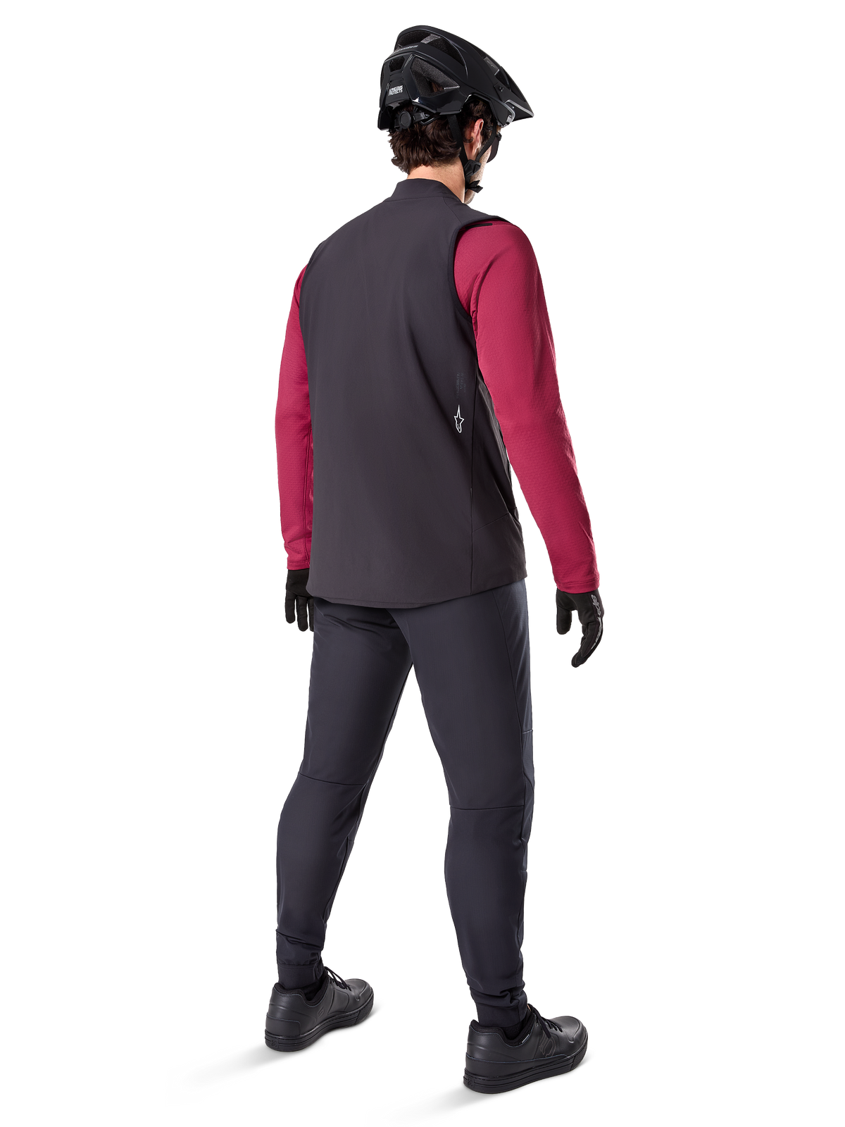 Alpinestars A-Dura Thermal Vest, Black cycling vest, shown from the back on a model wearing a maroon long-sleeve jersey and black cycling pants, paired with a black mountain bike helmet and gloves, technical gear for cold-weather riding