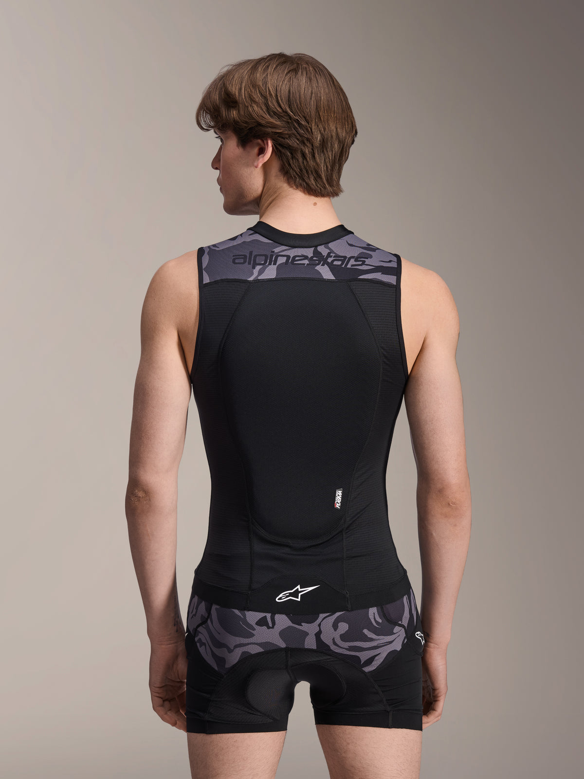 Alpinestars A-Motion Plasma beschermvest, Black Camo, achteraanzicht op mannelijk model, voorzien van een ademende mesh-constructie met een geïntegreerde Nucleon Plasma rugbeschermer, grijze camouflage-accenten op de schouders en taille, en Alpinestars branding.
