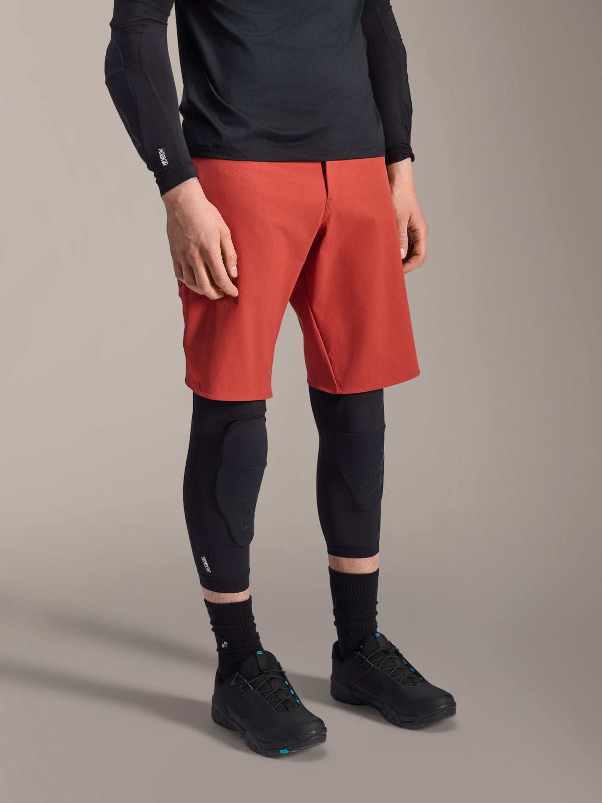 Alpinestars A-Motion Plasma Knee Sleeve, MTB kniebeschermer, zwart, gedragen met een rode short en zwarte mountainbikeschoenen, laag profiel instapontwerp met voorgevormde beschermende pads en ademend mesh