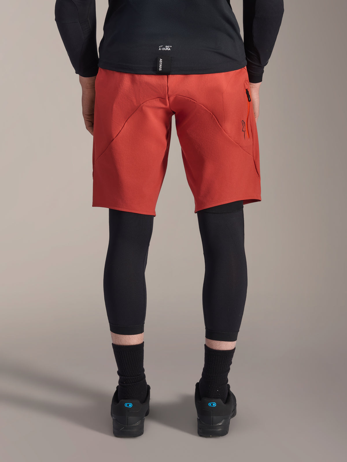 Alpinestars A-Motion Plasma Knee Sleeve, zwarte MTB-kniebeschermers, achteraanzicht gedragen onder een rode mountainbikebroek met een zwart fietsshirt en technische fietsschoenen, beschermende uitrusting voor mountainbiken