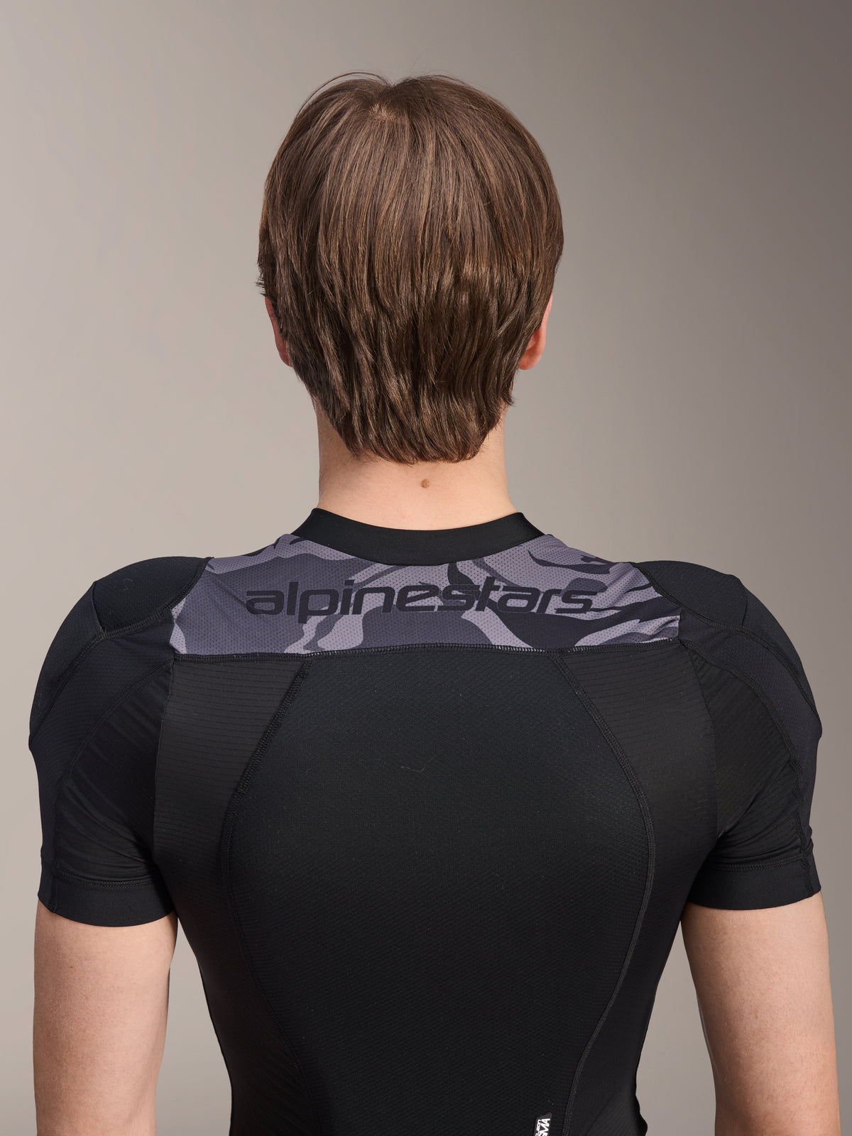Alpinestars A-Motion Plasma Protection Jacket - korte mouwen, achteraanzicht van het bovenlichaam, zwart met grijs camouflagepaneel over de schouders met Alpinestars-logo, ademende stretch mesh-constructie voor MTB-bescherming