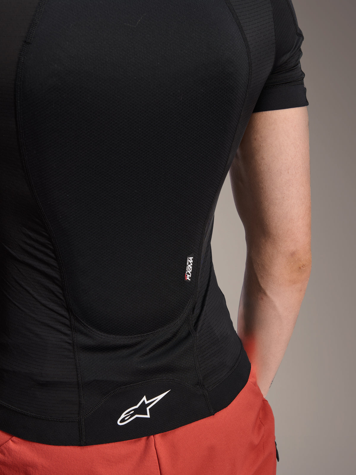 Alpinestars A-Motion Plasma beschermjas met korte mouwen, Black Camo, detailaanzicht van de achterkant met Nucleon PLASMA branding en wit Alpinestars logo op de zoom, ademende stretch mesh constructie voor MTB-bescherming