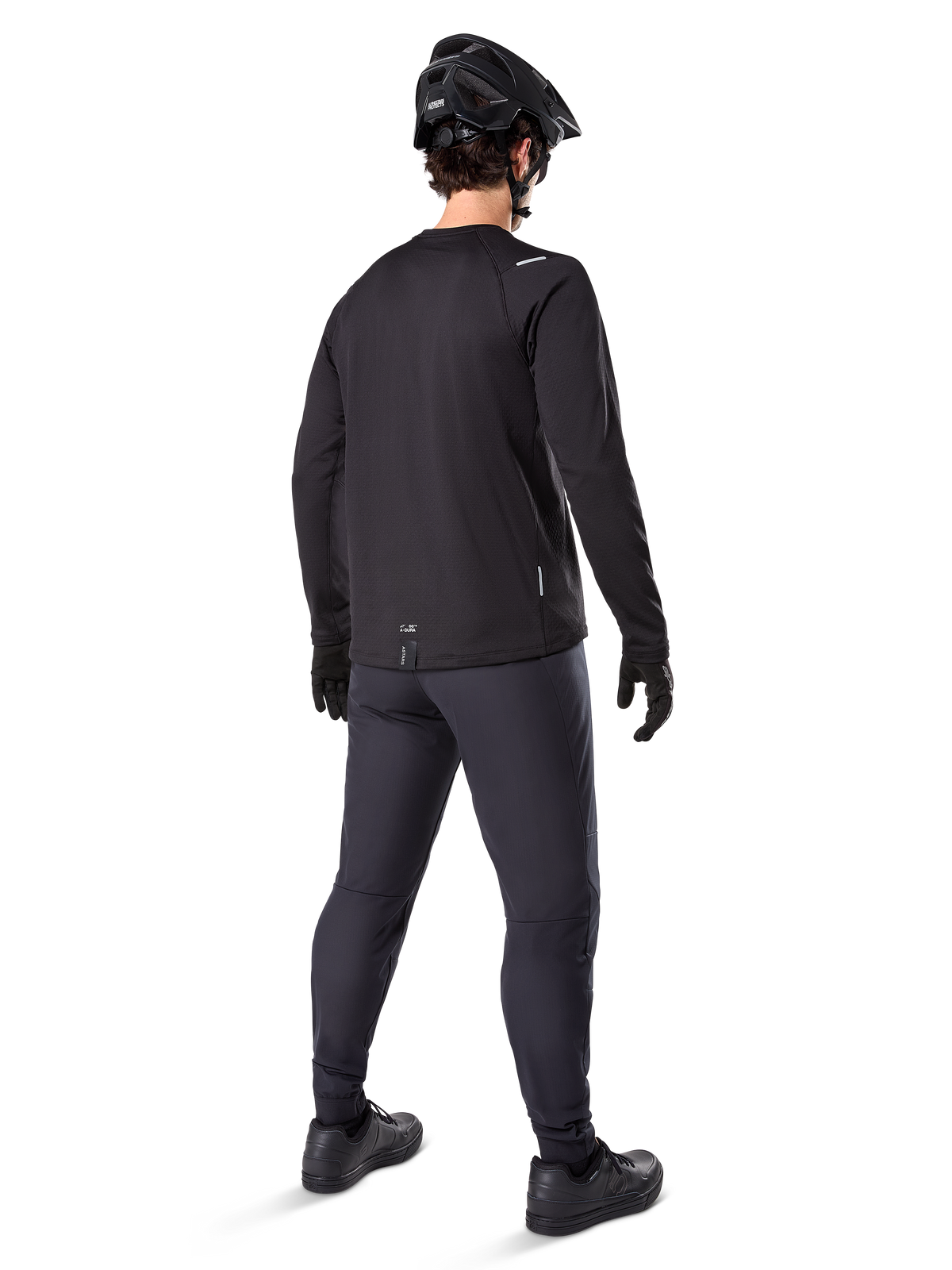 Pantalon thermique Alpinestars A-Dura, pantalon de VTT, noir, vu de dos, porté avec un maillot à manches longues assorti, un casque de VTT noir et des gants, équipement de cyclisme technique pour temps froid