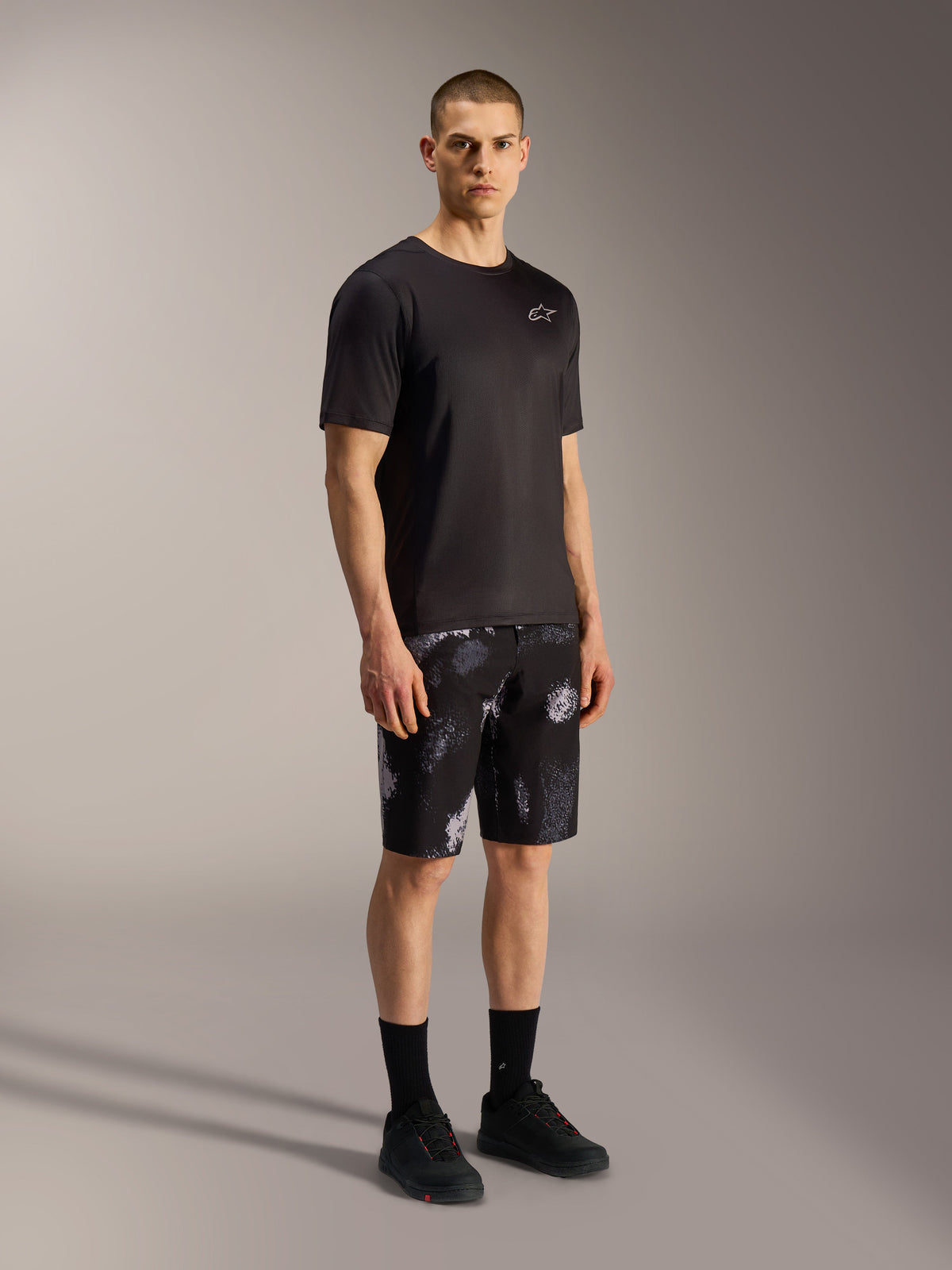 Short Alpinestars A-Dura Ride Black Camo, motif camouflage gris, porté avec un maillot et des chaussures de VTT noirs.